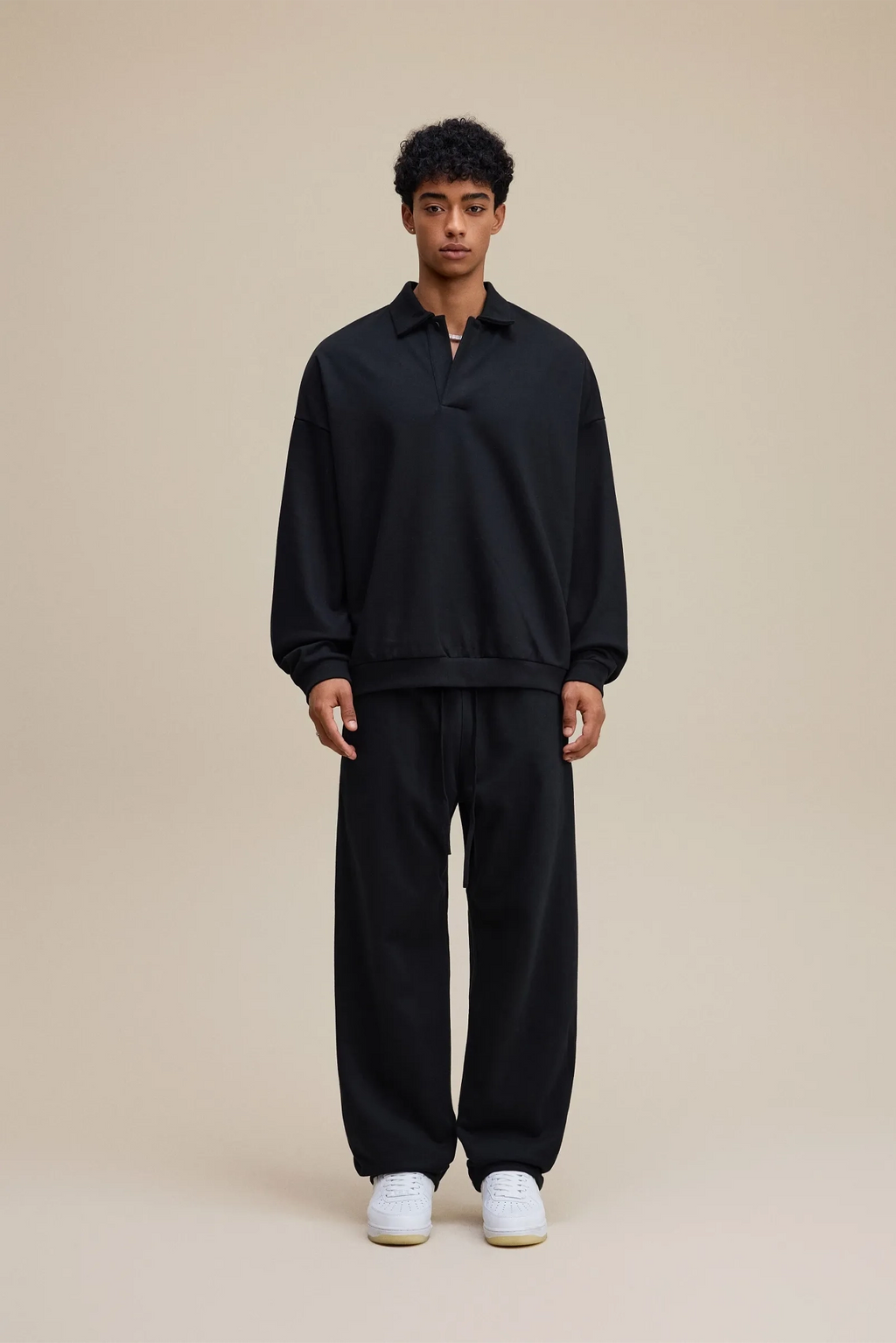 Person wearing a black outfit with white shoes on a beige background