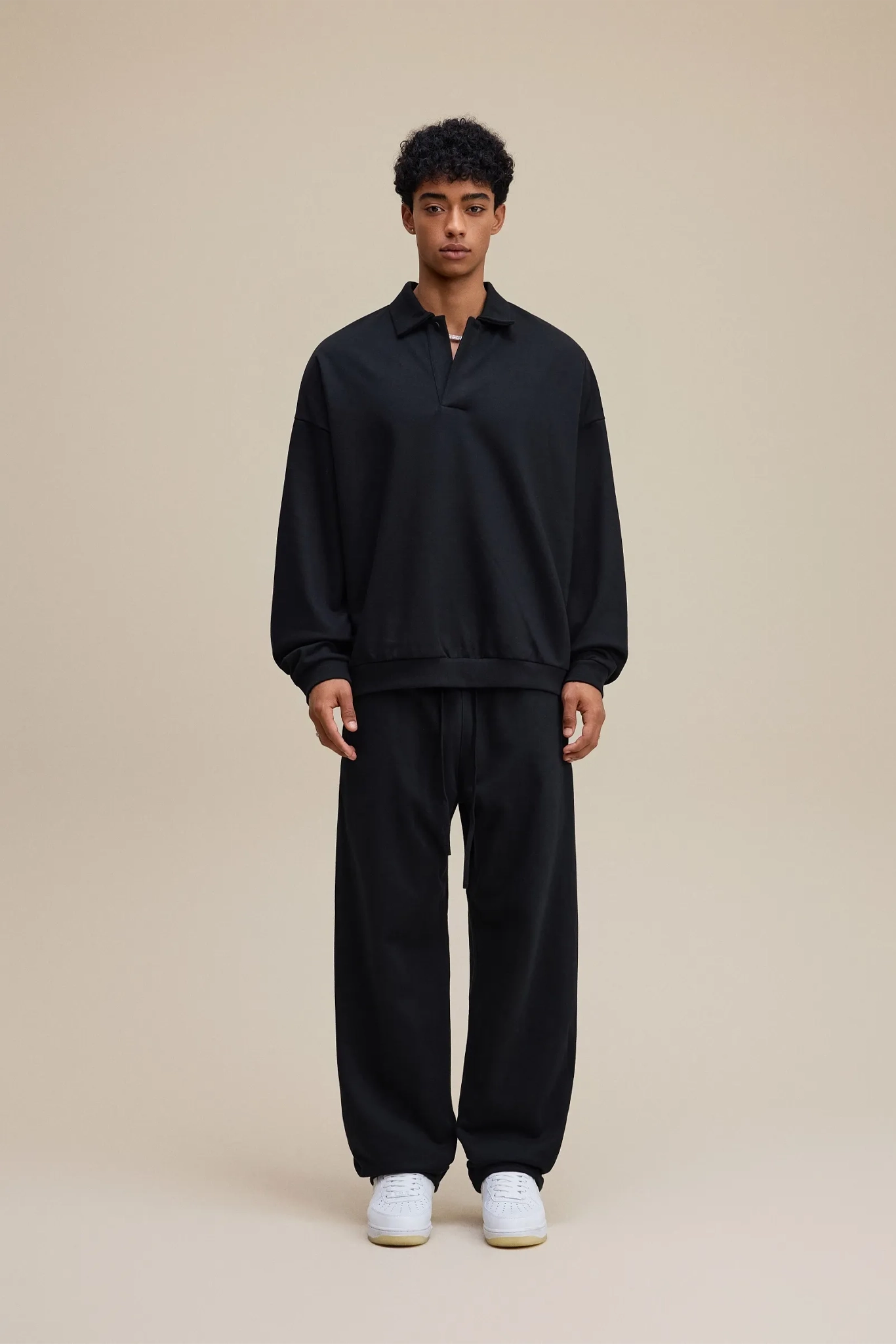 Person wearing a black outfit with white shoes on a beige background