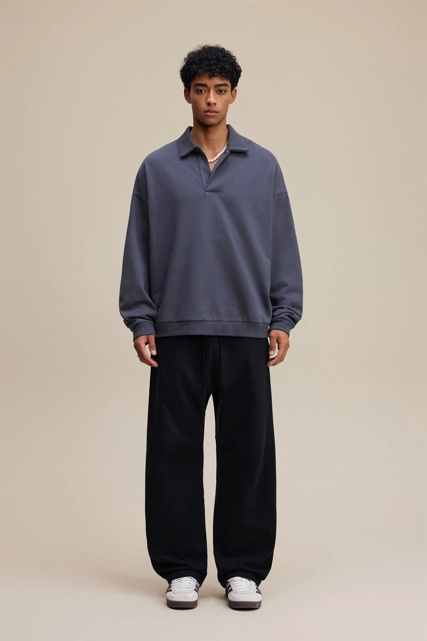 Person wearing a gray sweater and black pants on a beige background