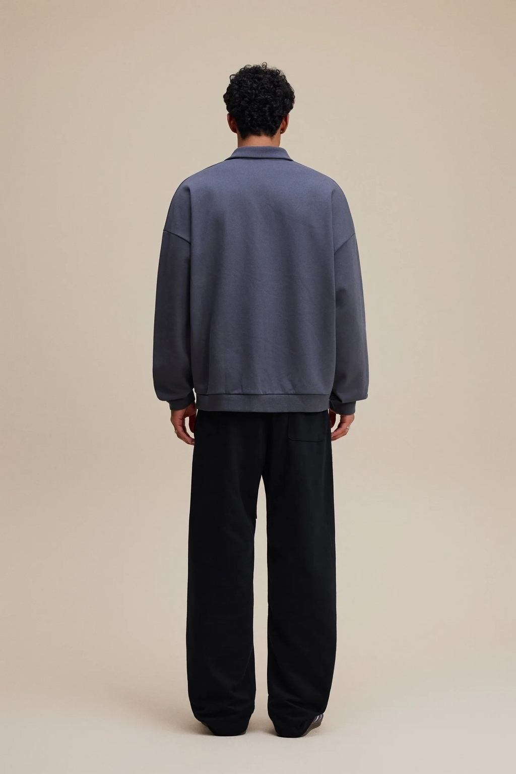 Person wearing a blue sweater and black pants on a beige background