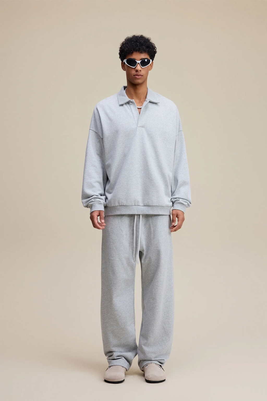 Person wearing a light gray outfit with sunglasses on a beige background