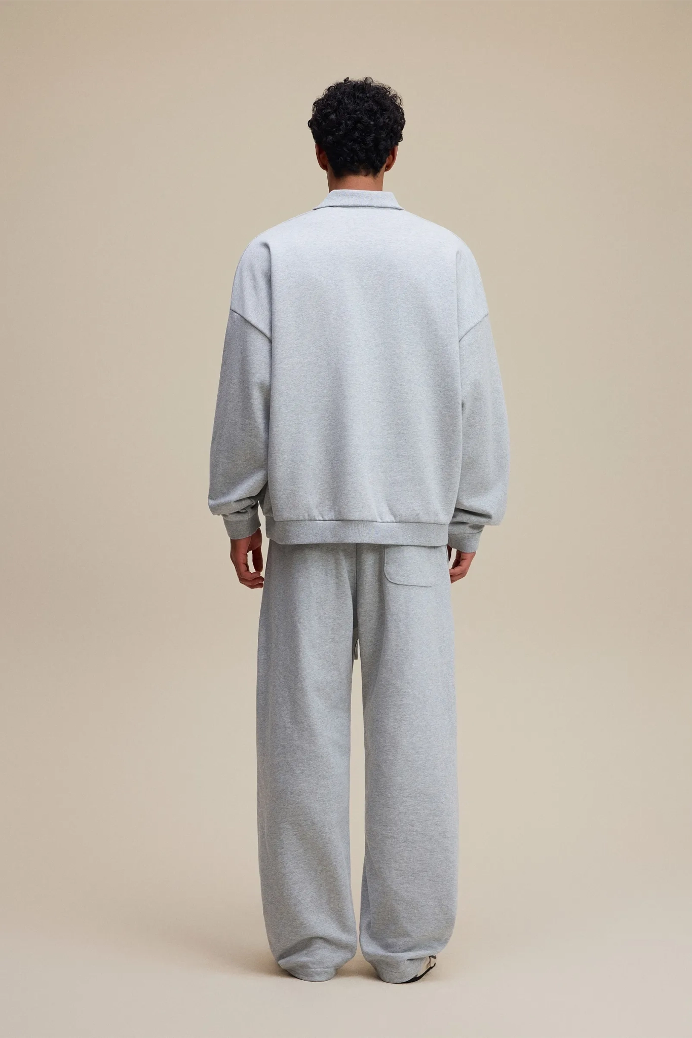 Person wearing a gray tracksuit standing against a beige background