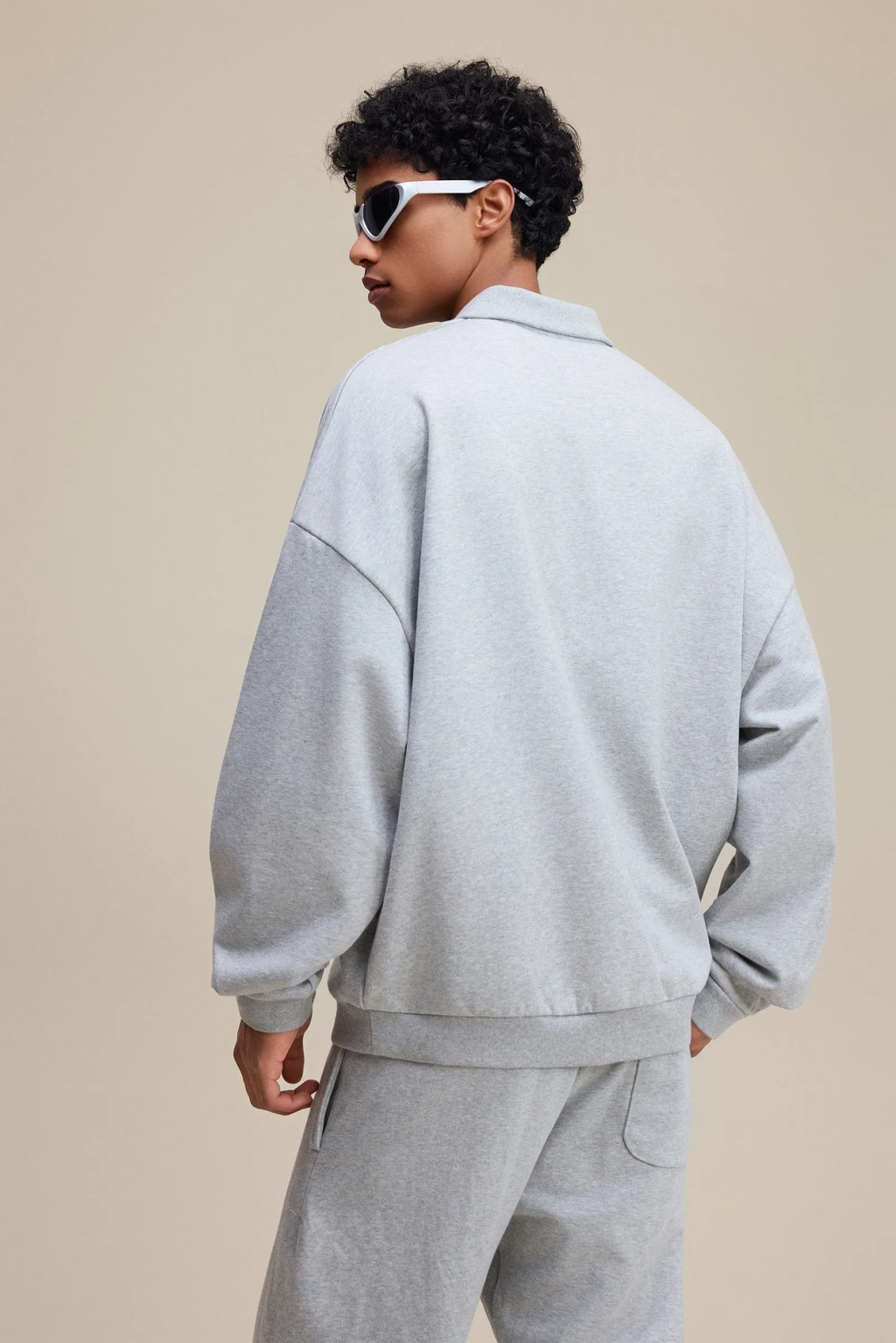 Person wearing a gray tracksuit and sunglasses on a beige background