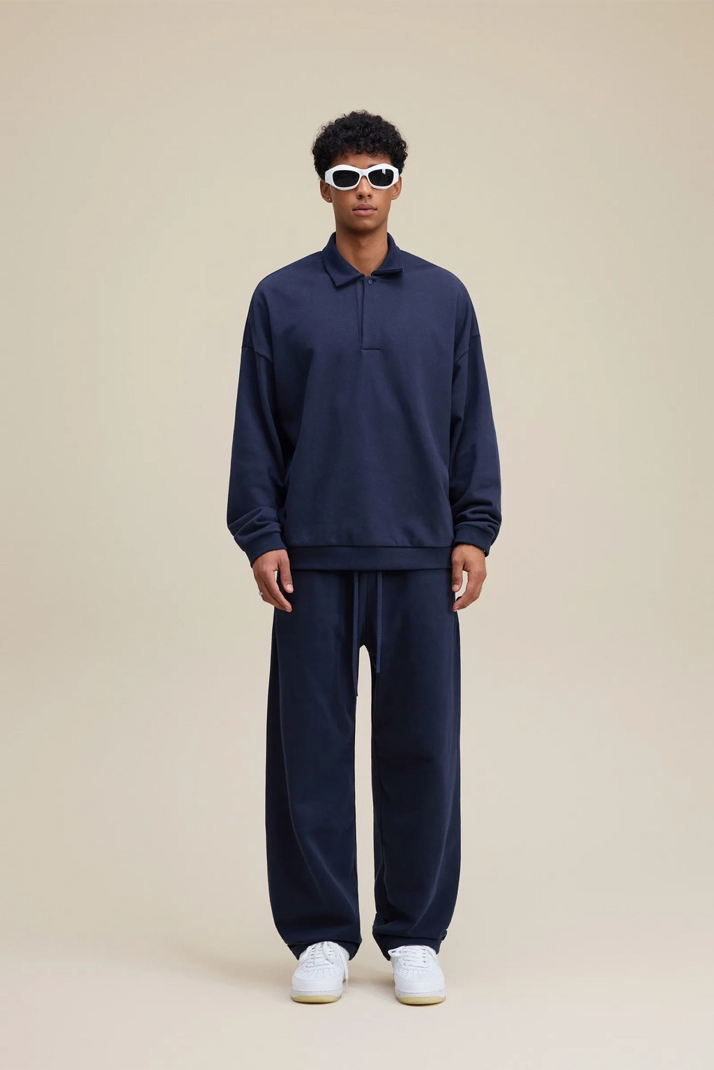 Person wearing a navy tracksuit with sunglasses on a beige background
