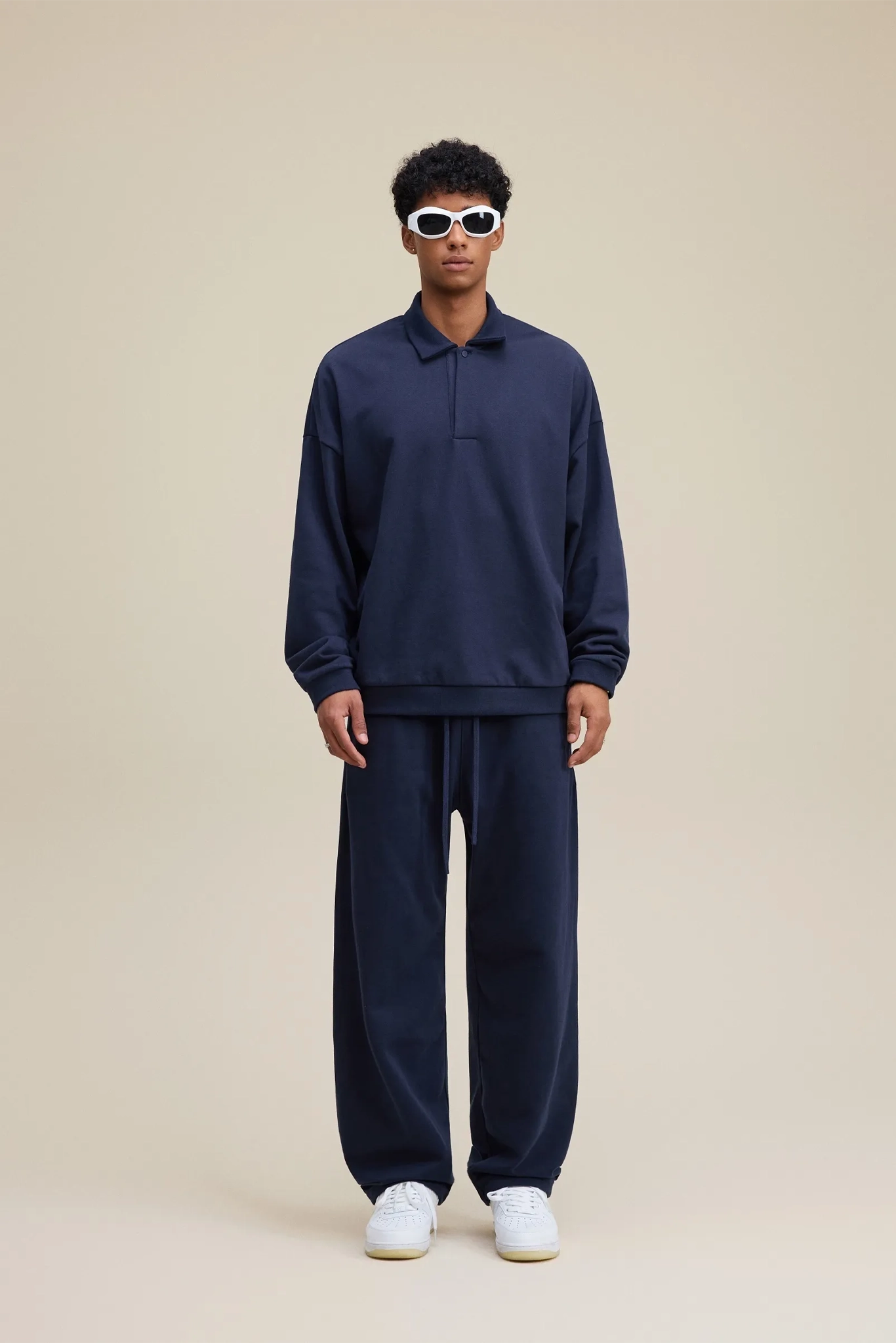 Person wearing a navy tracksuit with sunglasses on a beige background