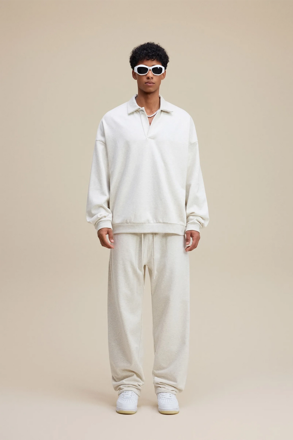 Person wearing a white outfit with sunglasses on a beige background