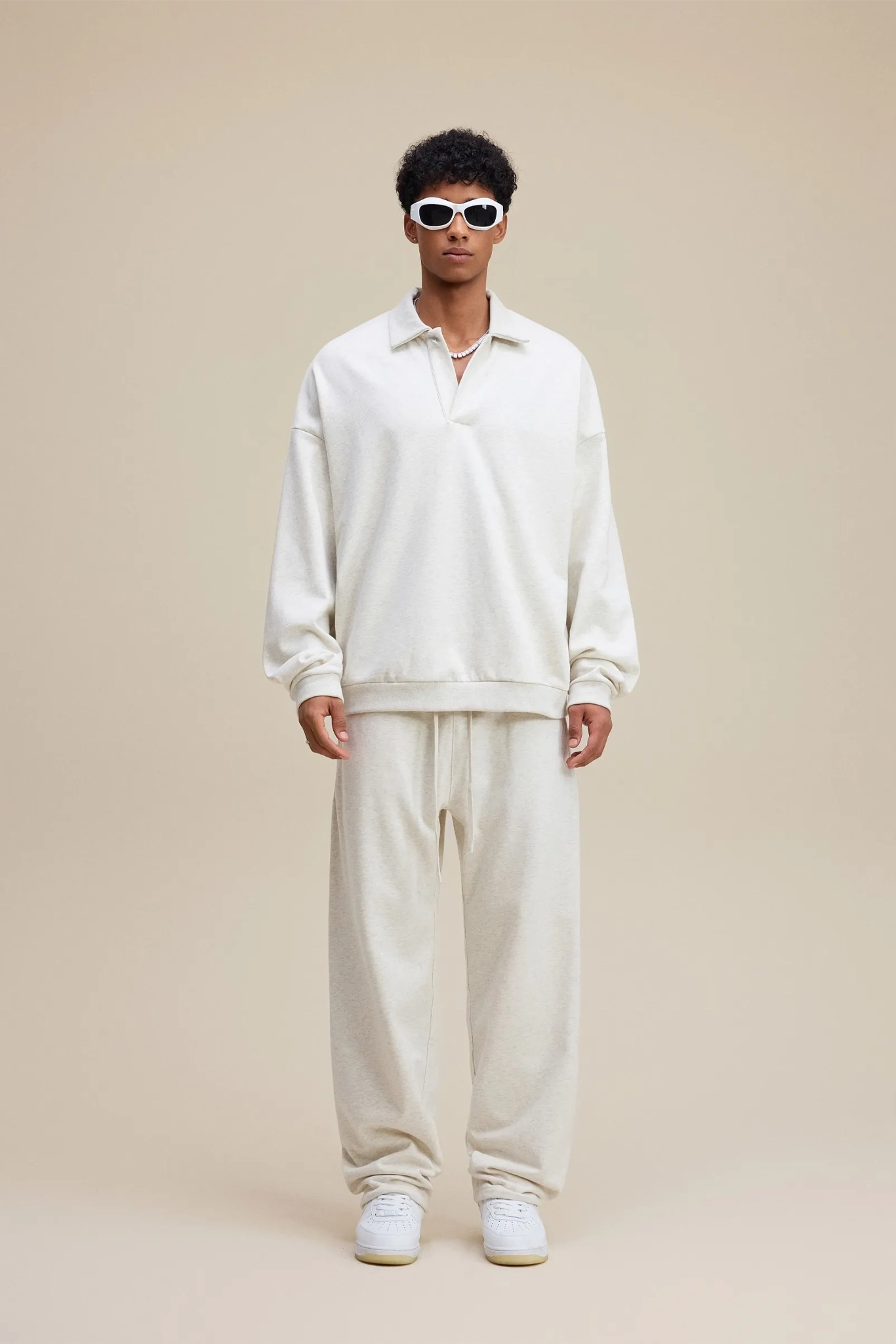 Person wearing a white outfit with sunglasses on a beige background