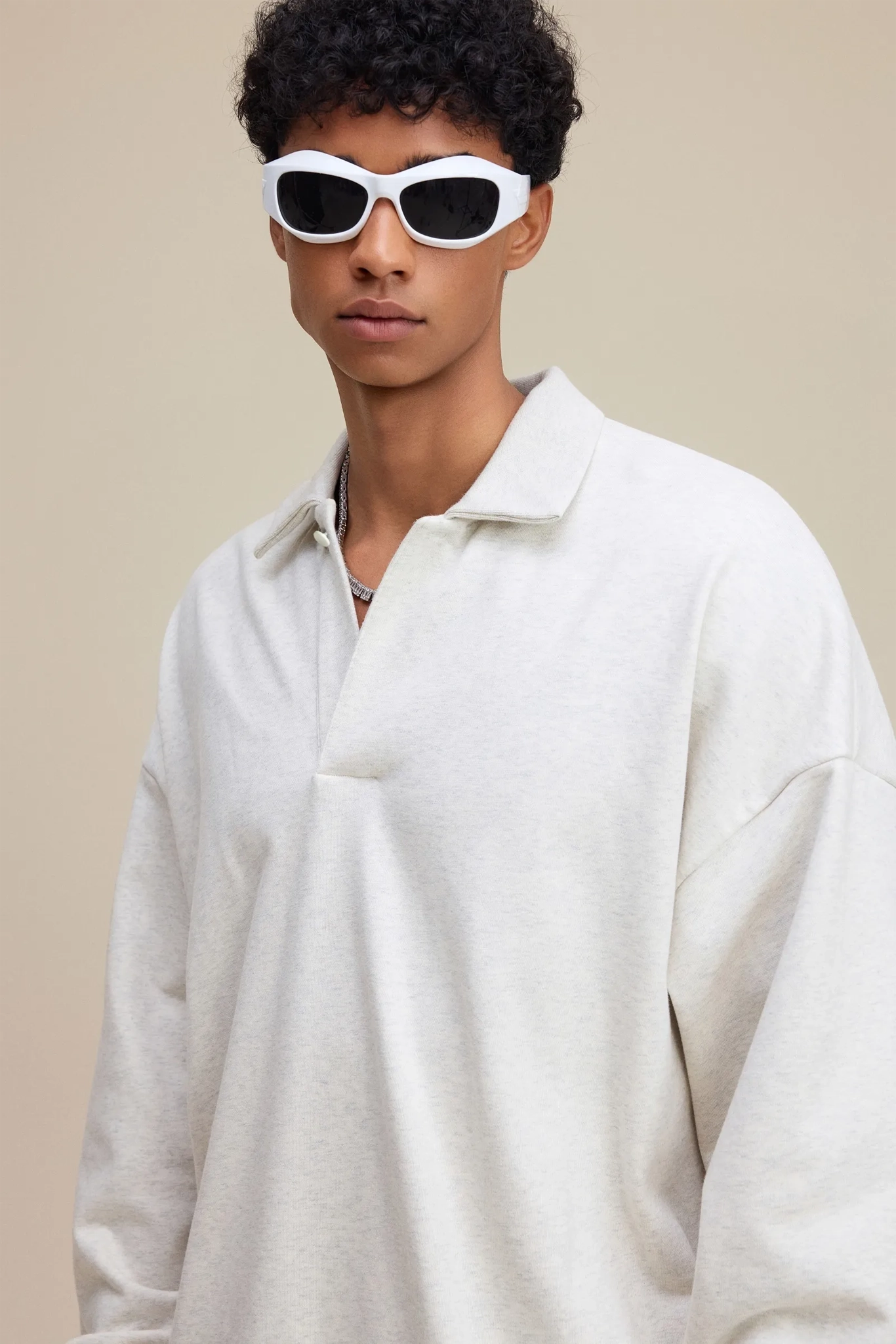 Person wearing white sunglasses and a light gray sweater against a beige background