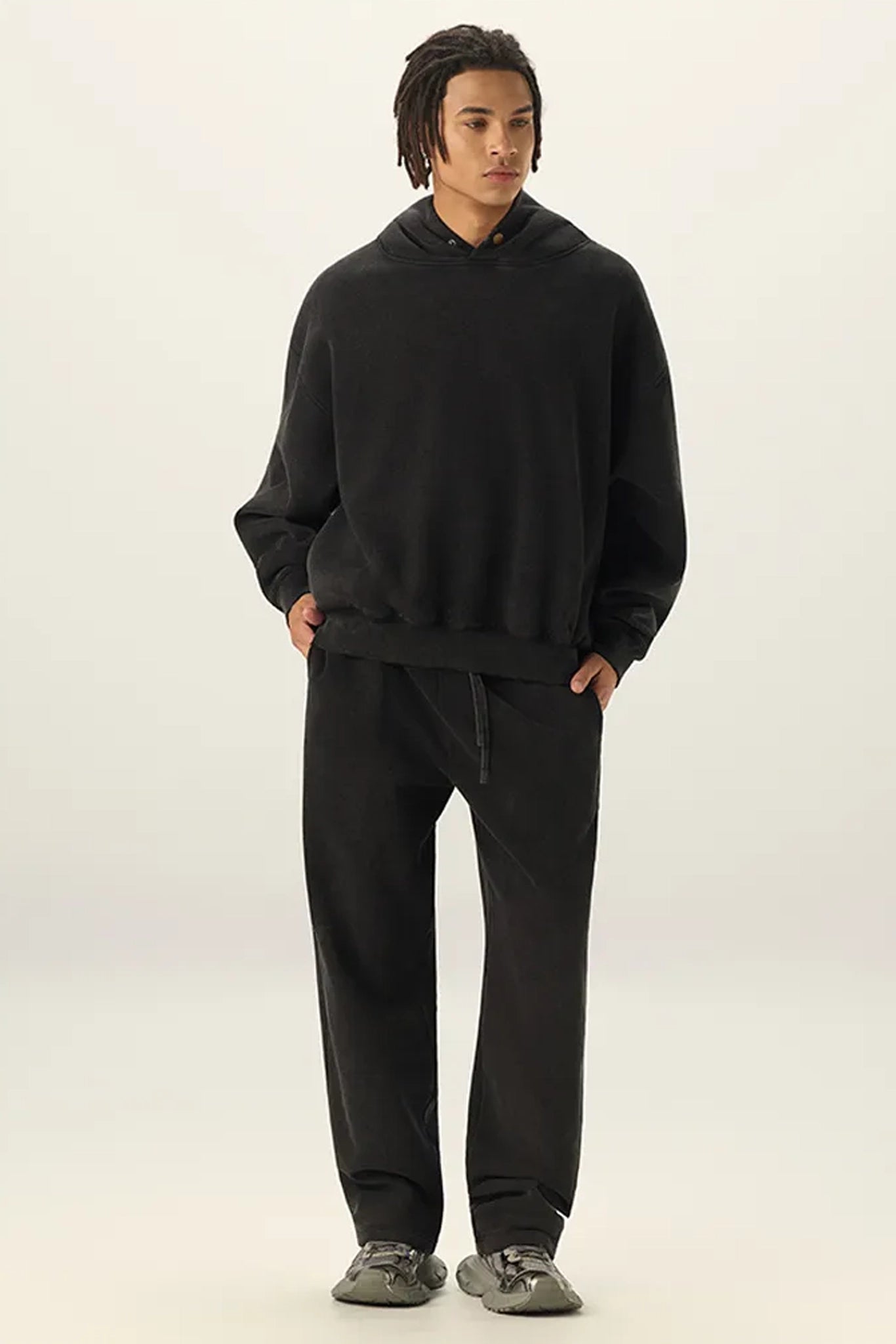 Person wearing a black hoodie and pants on a white background