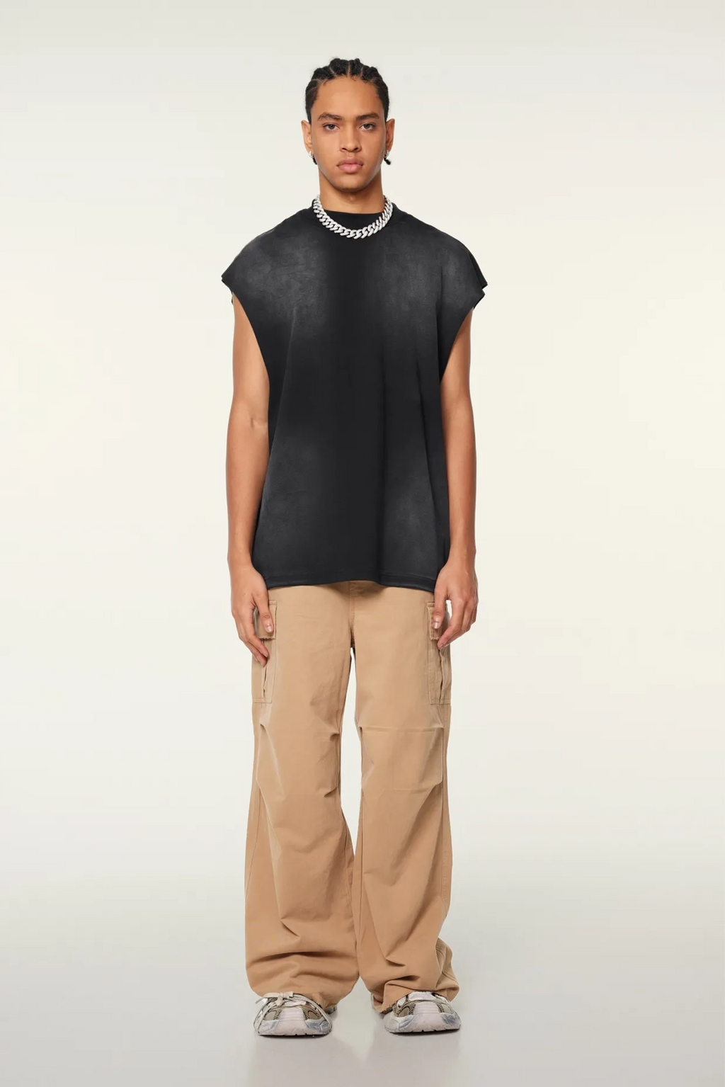 Person wearing a black sleeveless top and beige pants on a white background