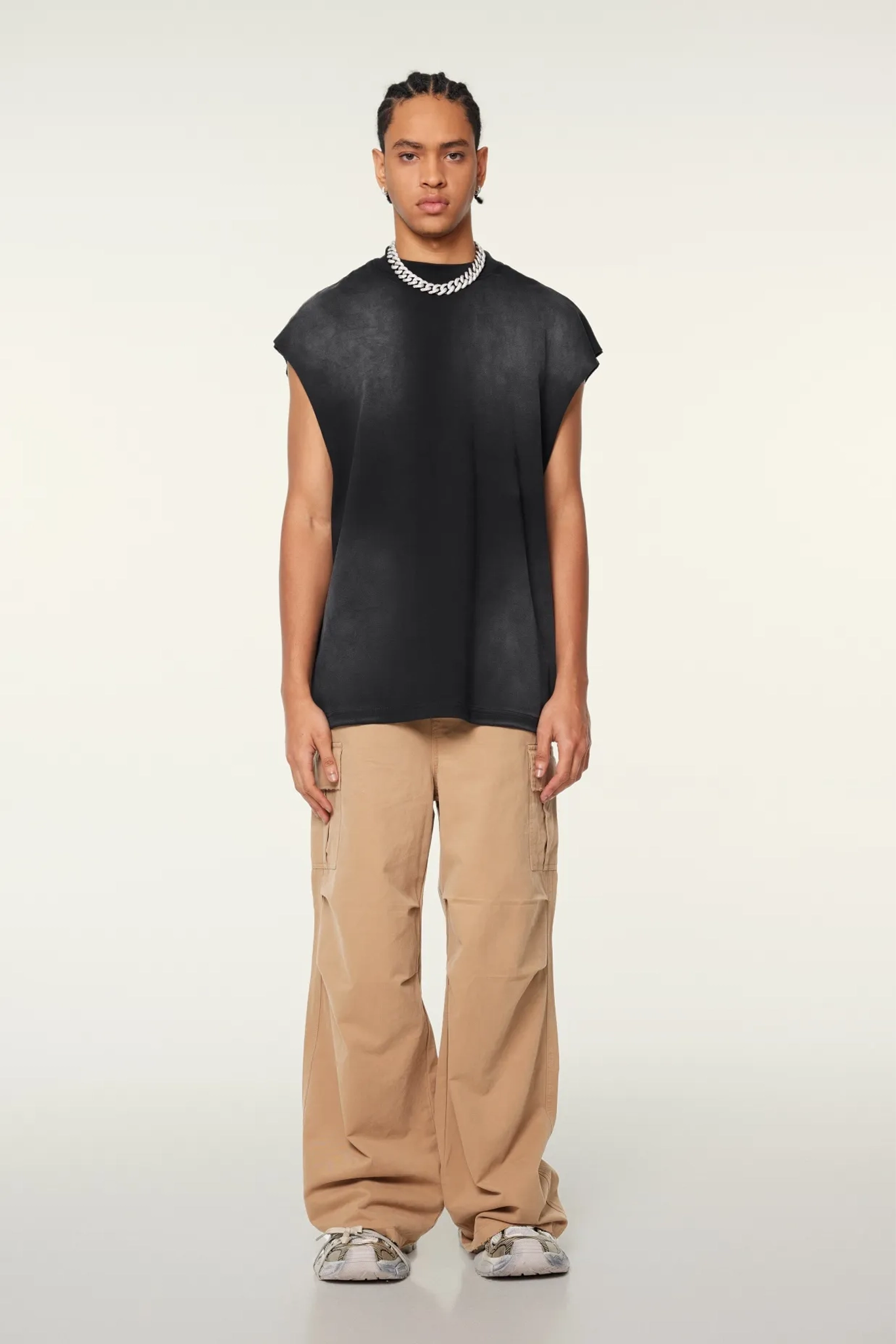 Person wearing a black sleeveless top and beige pants on a white background