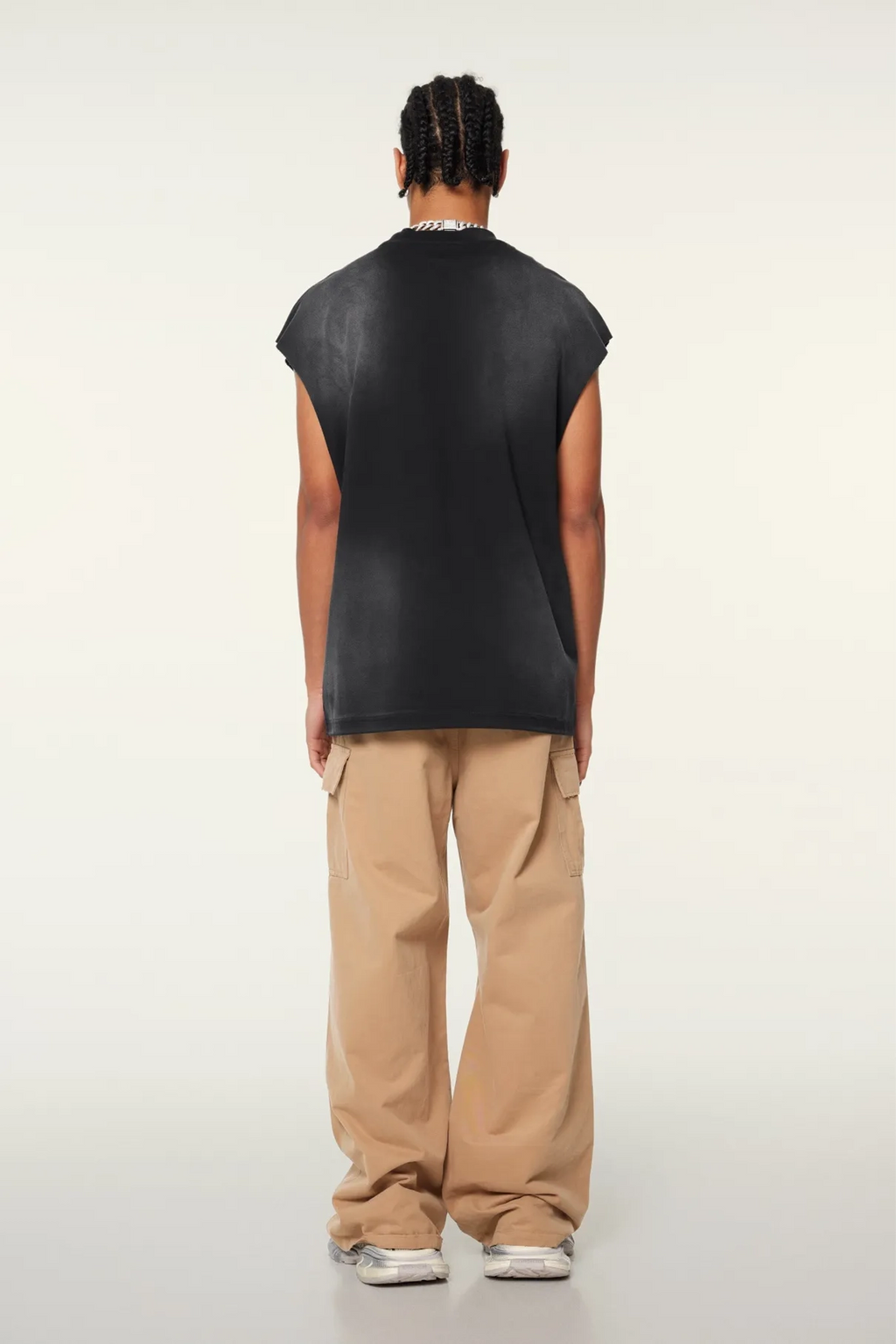 Person wearing a black sleeveless shirt and beige pants on a white background