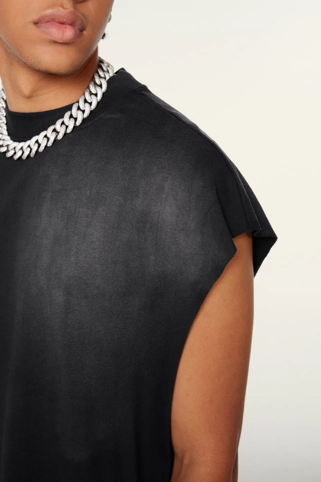 Person wearing a black sleeveless top and silver chain necklace on a white background