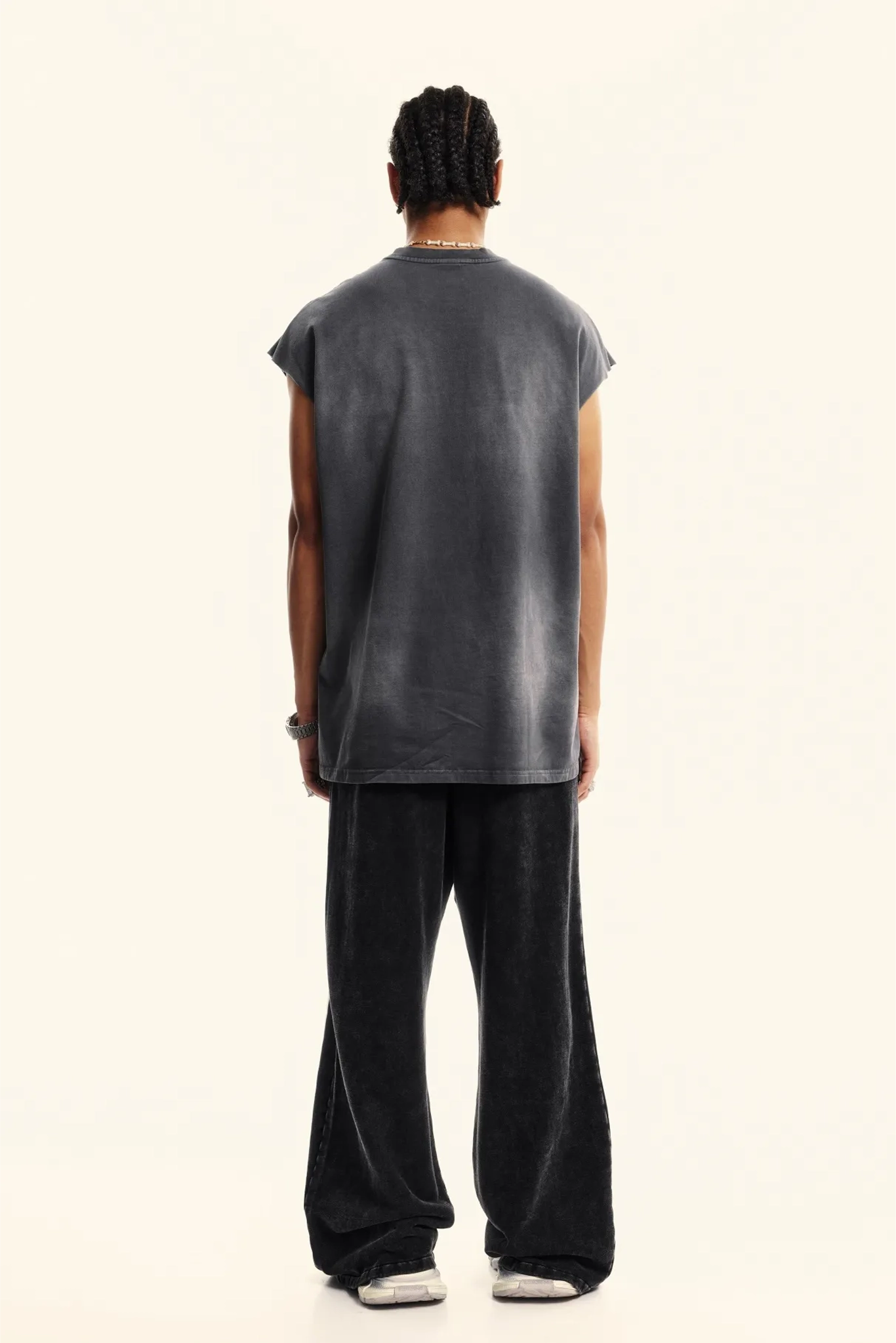 Person wearing a sleeveless gray shirt and black pants on a white background