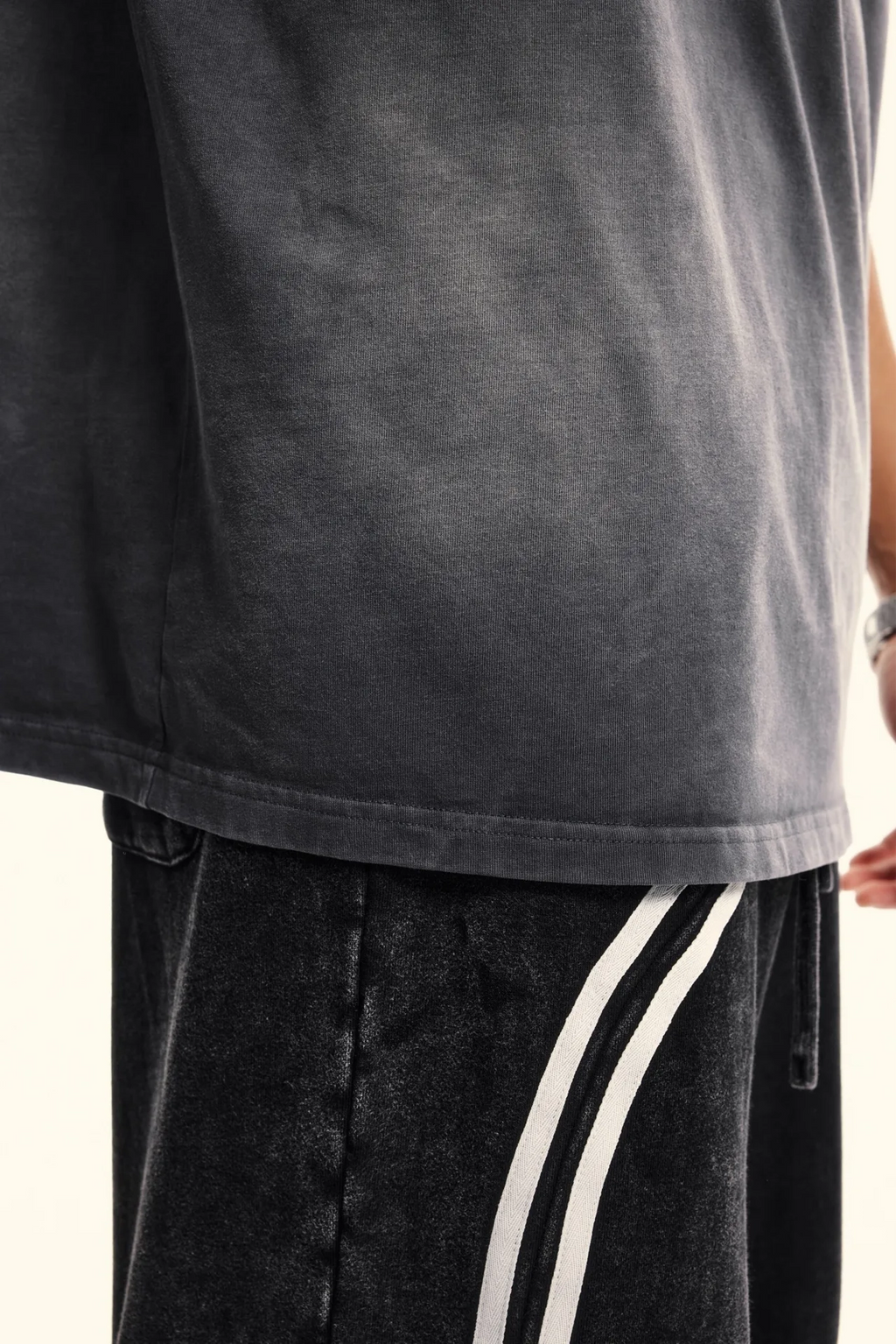 Person wearing a black t-shirt and black pants with white stripes on a light background