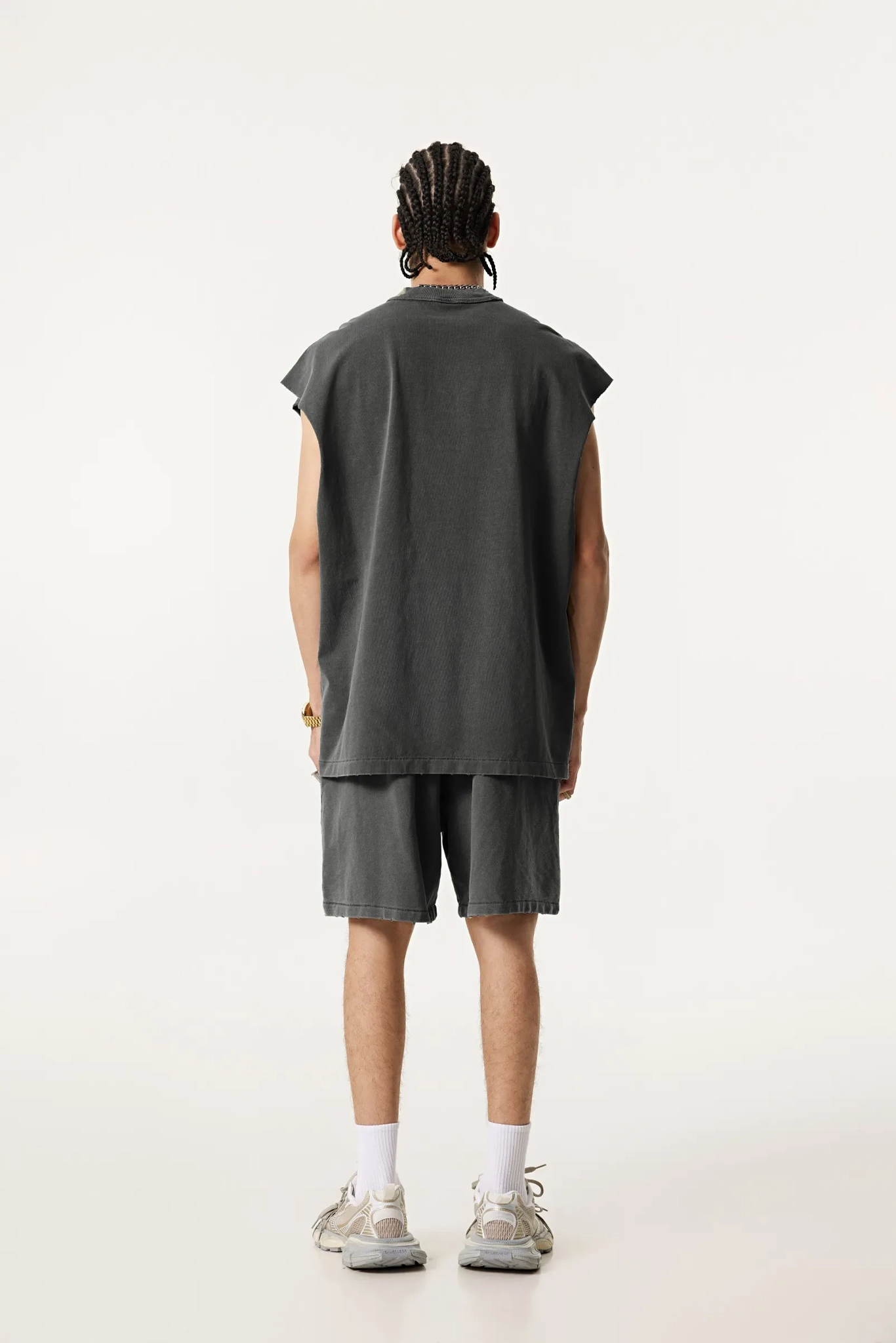 Person wearing a dark gray sleeveless shirt and shorts set on a white background