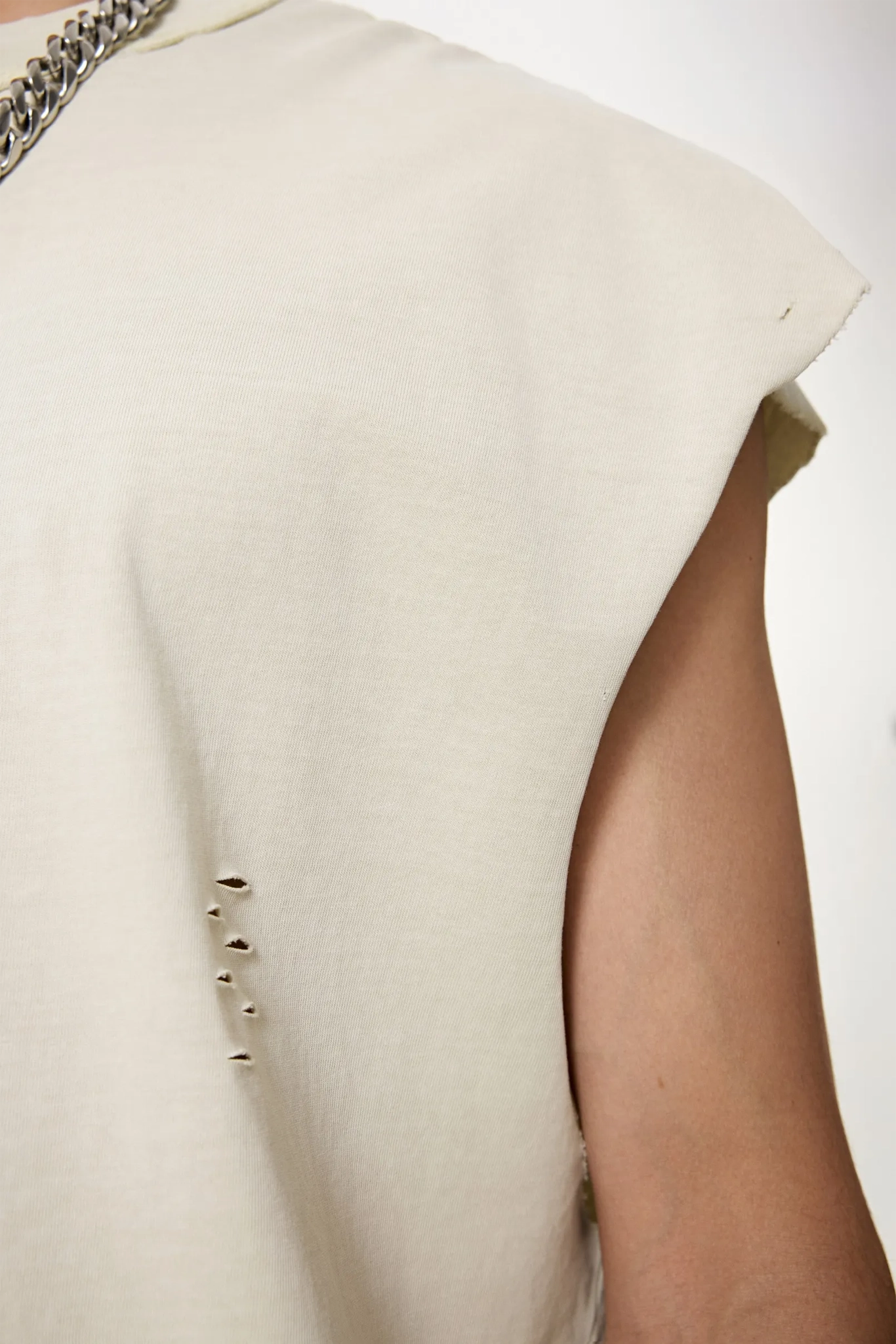 Close-up of a beige sleeveless garment with buttons on a white background