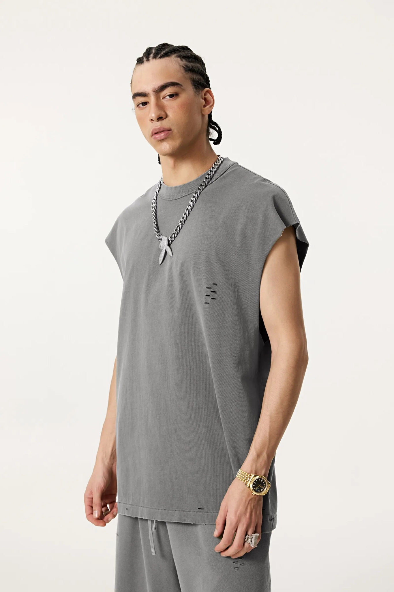 Man wearing a gray sleeveless shirt and pants with a necklace on a white background