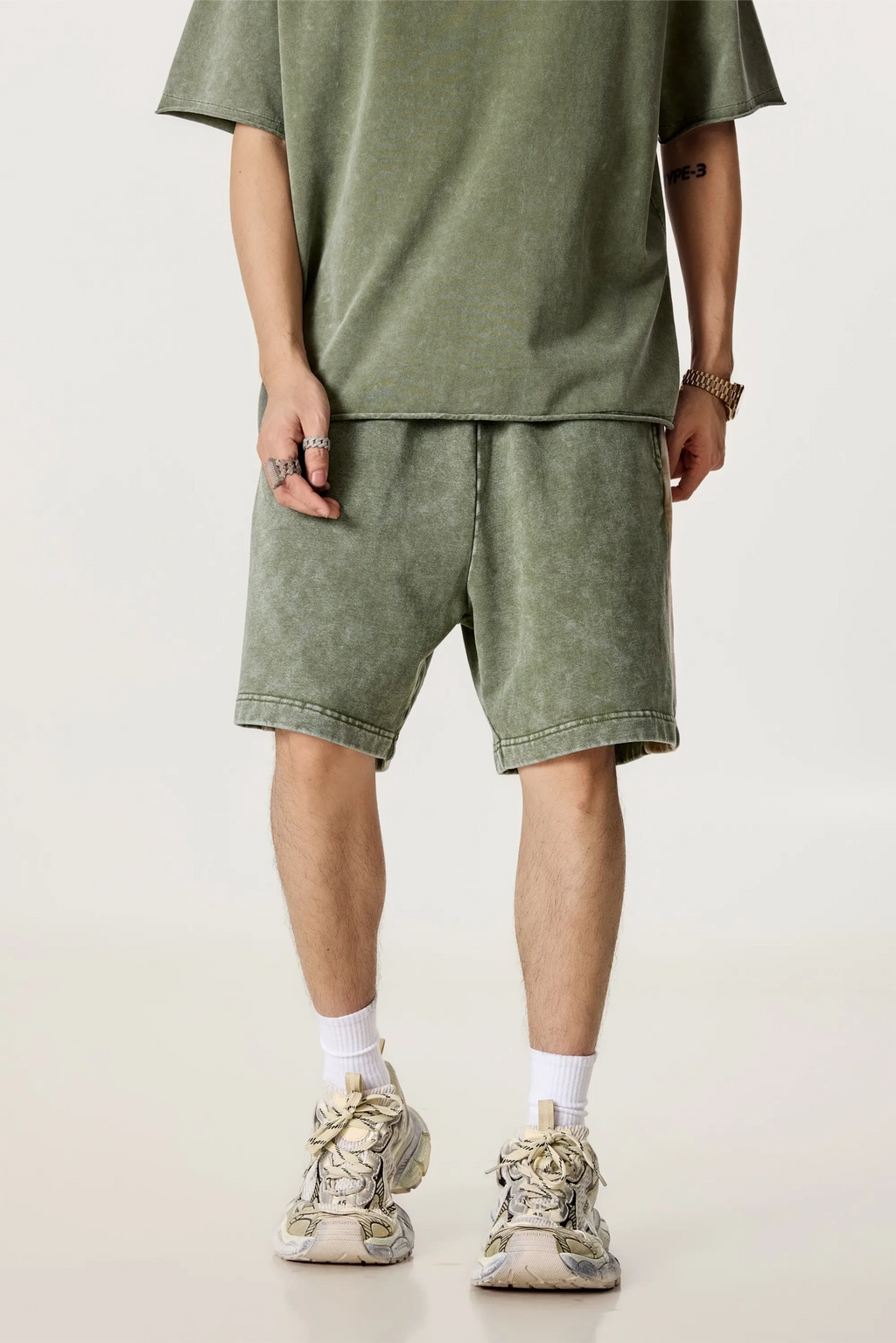 Person wearing a green t-shirt and shorts set with beige sneakers on a white background