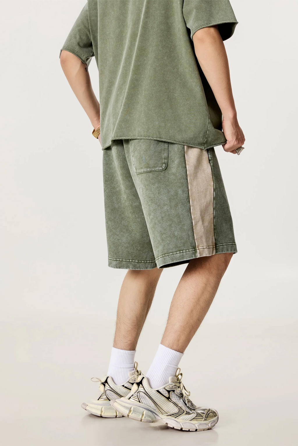 Person wearing a green oversized t-shirt and shorts with white socks and sneakers on a light background