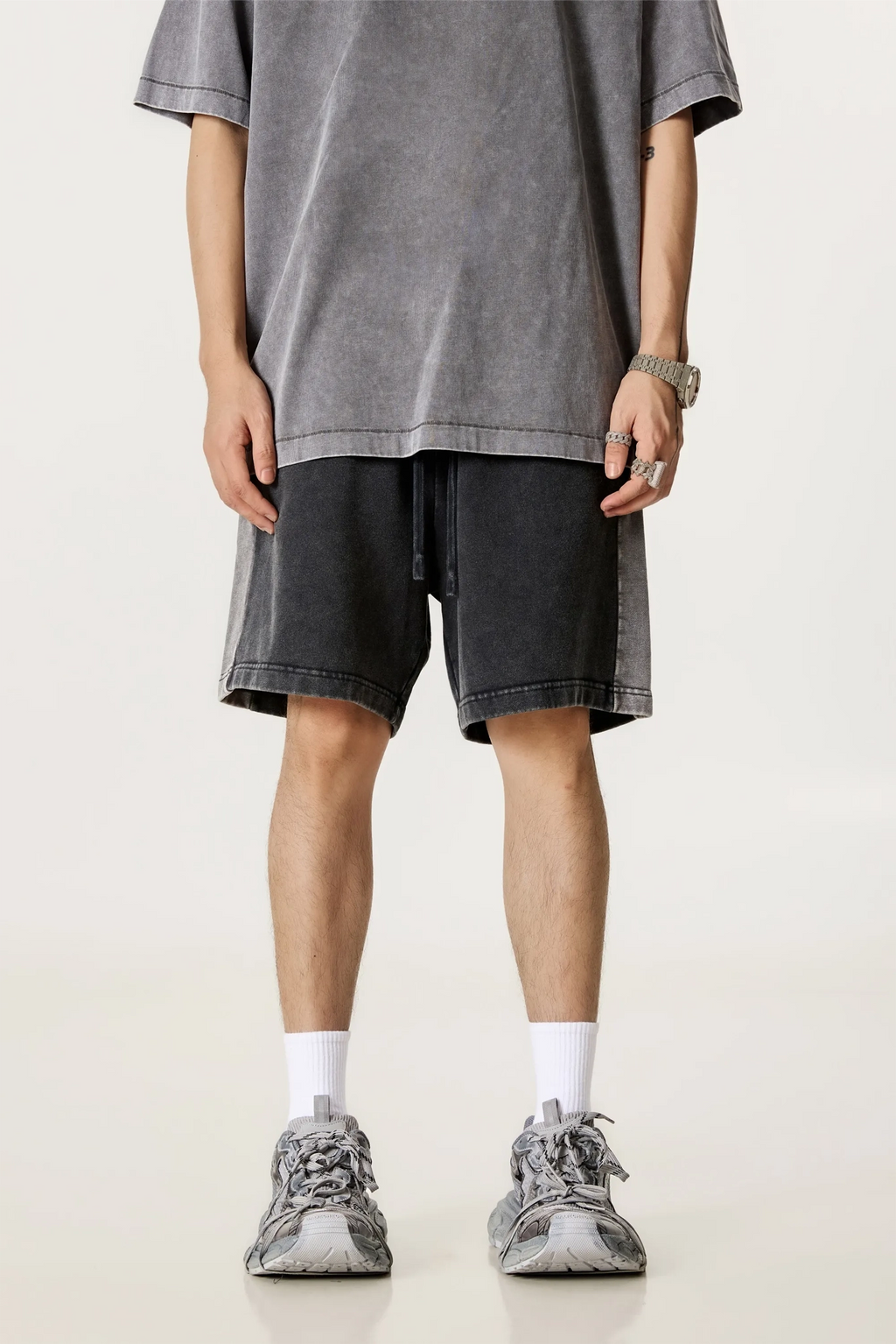 Person wearing a gray oversized t-shirt, black shorts, and gray sneakers on a plain background