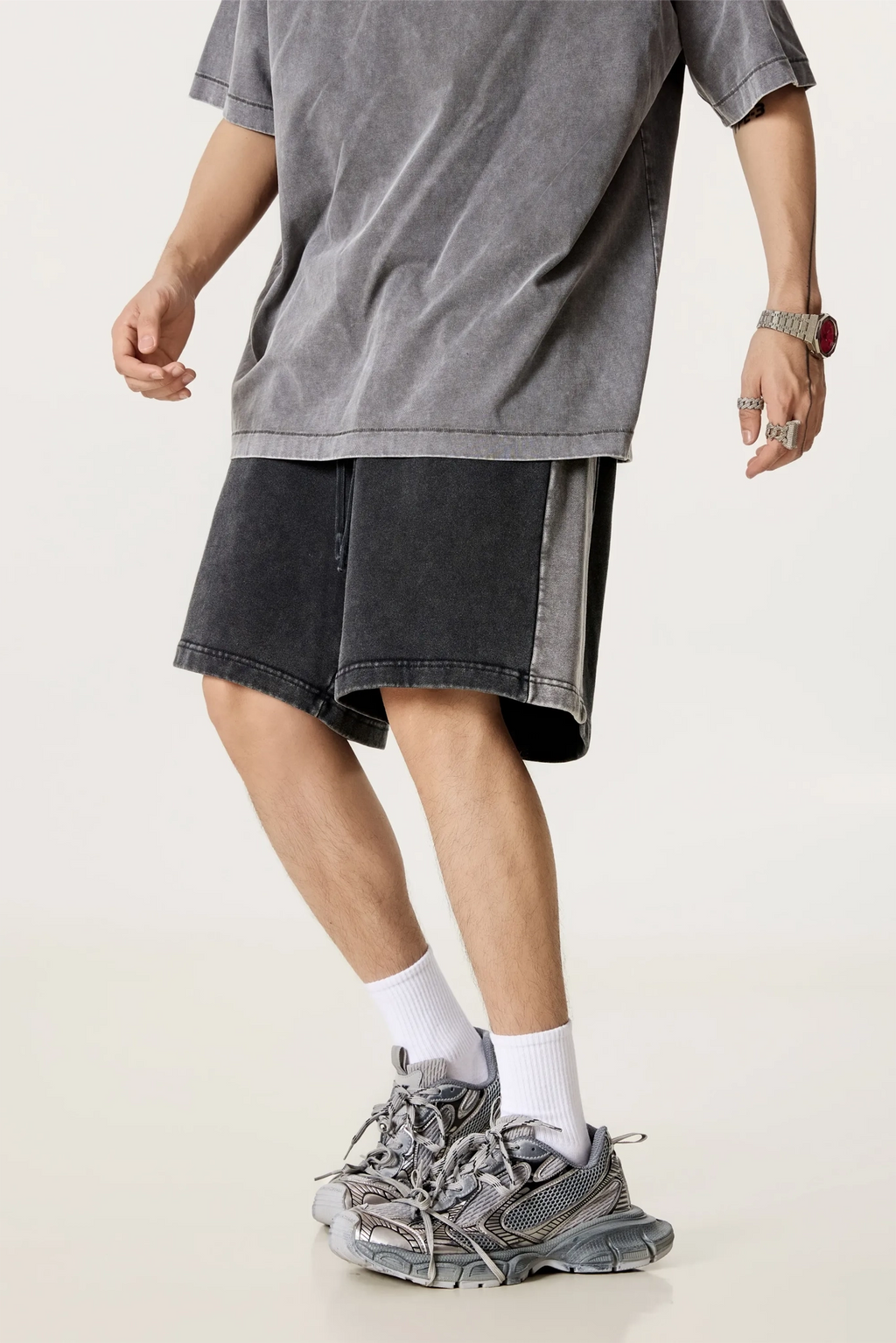 Person wearing a gray oversized t-shirt, black shorts, and gray sneakers on a white background