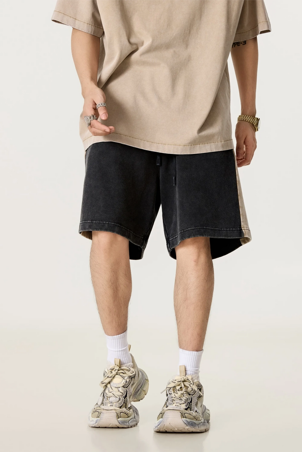 Person wearing a beige oversized t-shirt, black shorts, and white sneakers on a light background