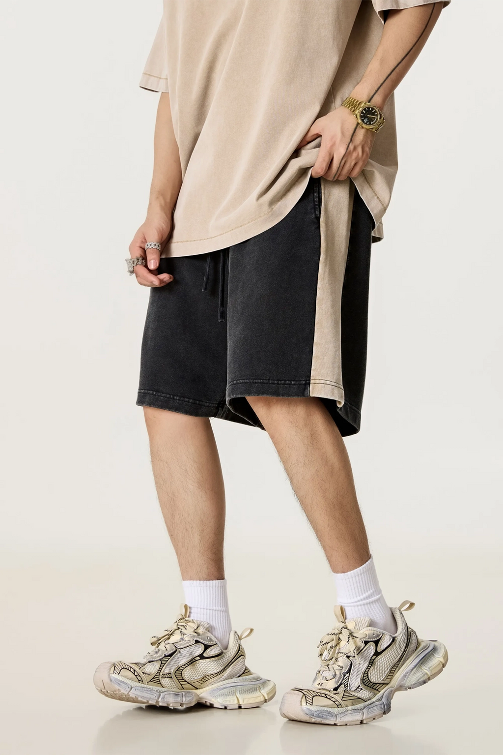 Person wearing a beige oversized shirt, black shorts, and white sneakers on a light background
