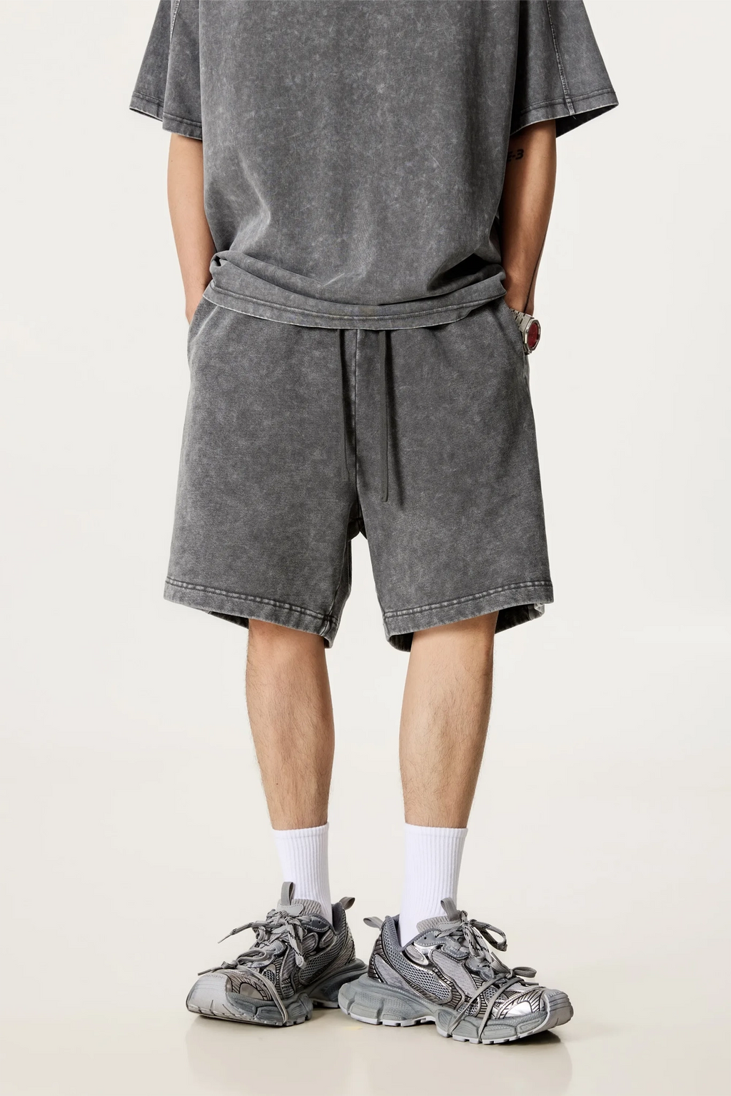 Person wearing gray shorts and t-shirt with sneakers on a white background