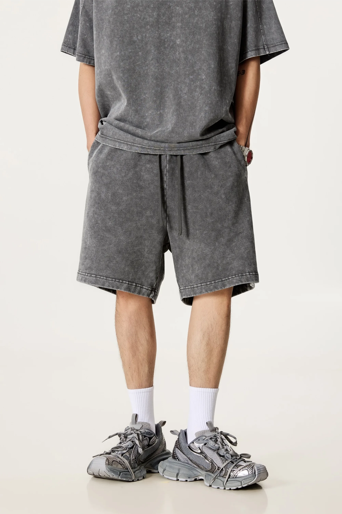 Person wearing gray shorts and t-shirt with sneakers on a white background