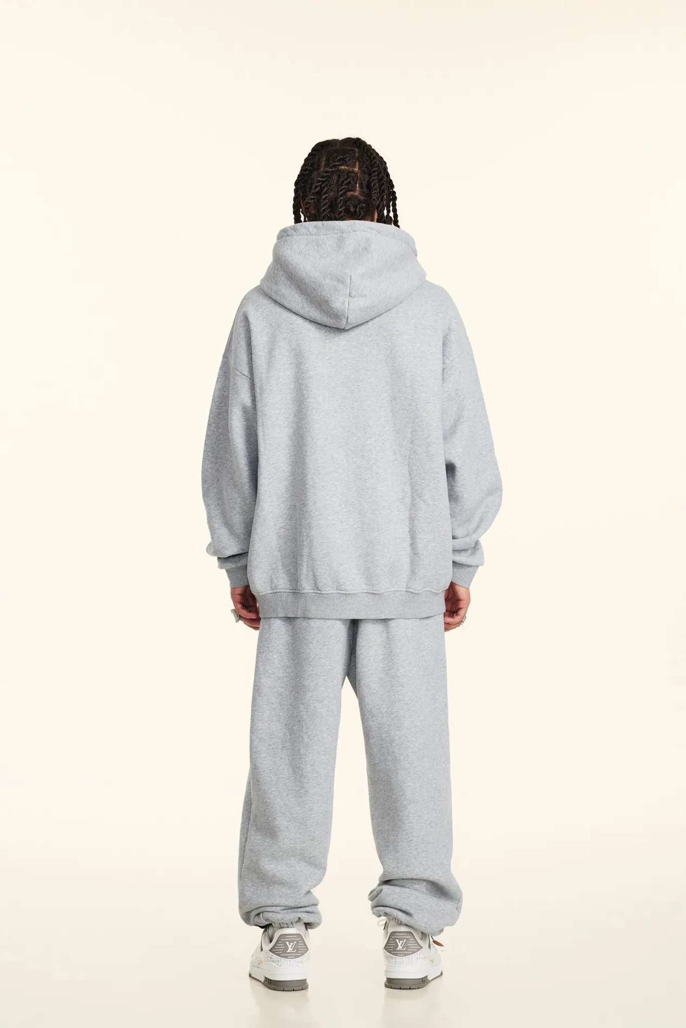 Person wearing a light gray hoodie and pants set on a white background