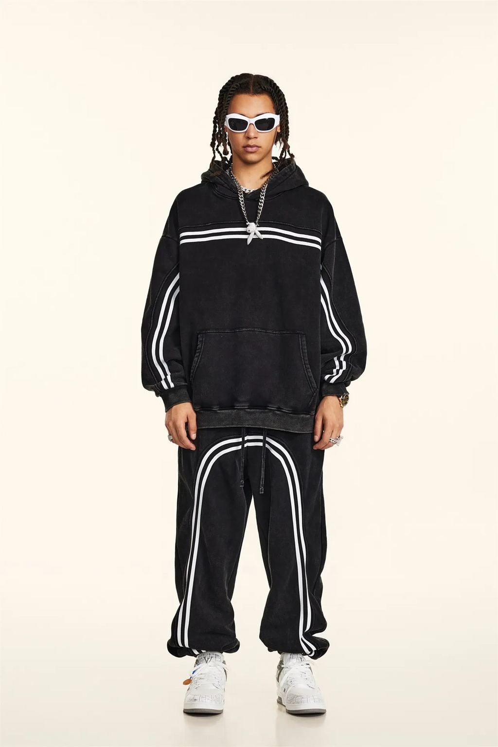 Person wearing a black hoodie and tracksuit with white stripes on a beige background