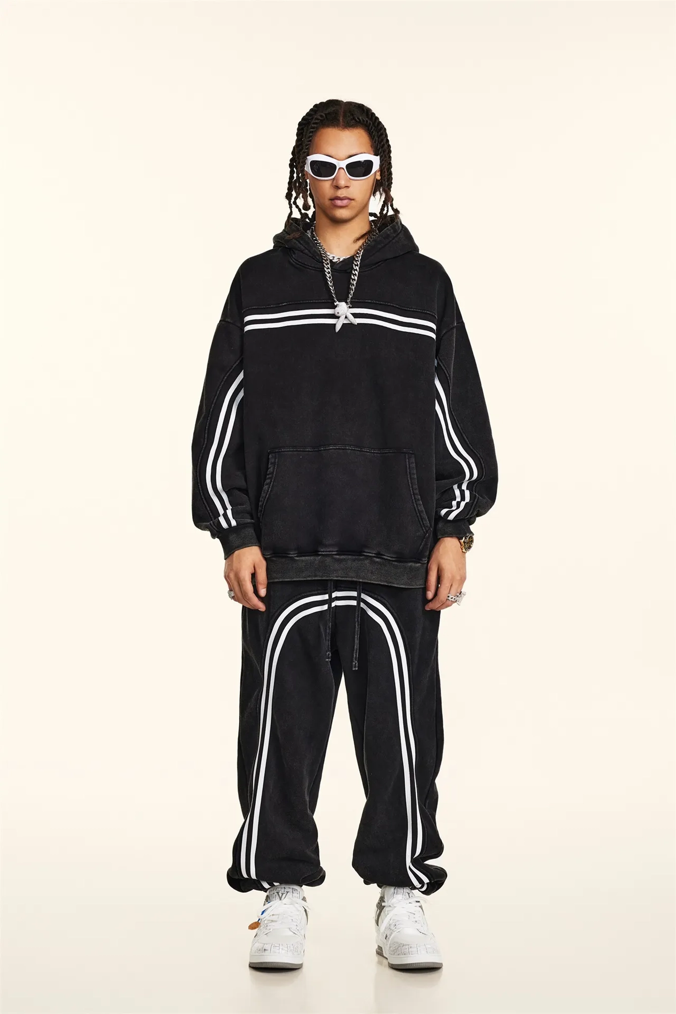 Person wearing a black hoodie and tracksuit with white stripes on a beige background