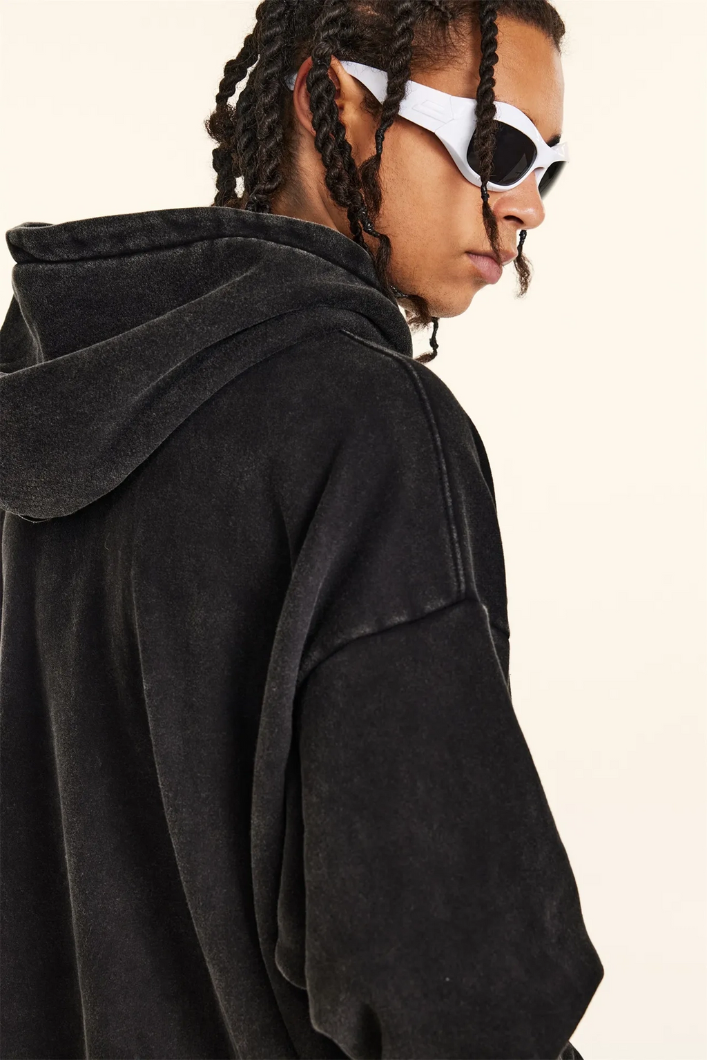 Person wearing a black hoodie and white sunglasses on a plain background