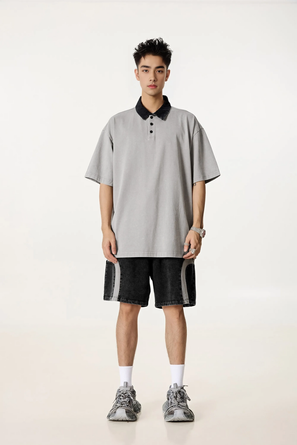 Person wearing a gray oversized polo shirt with a black collar and black shorts on a white background