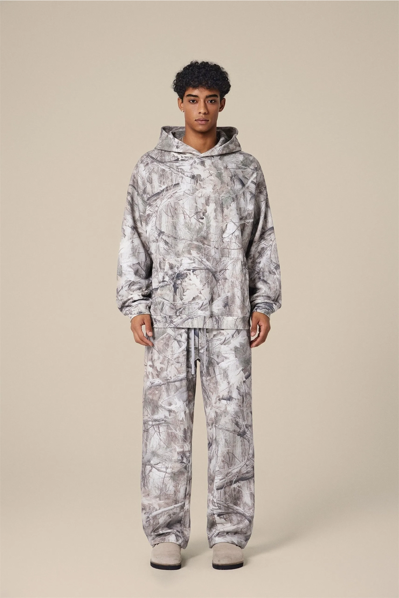 Person wearing a camouflage hoodie and pants on a beige background