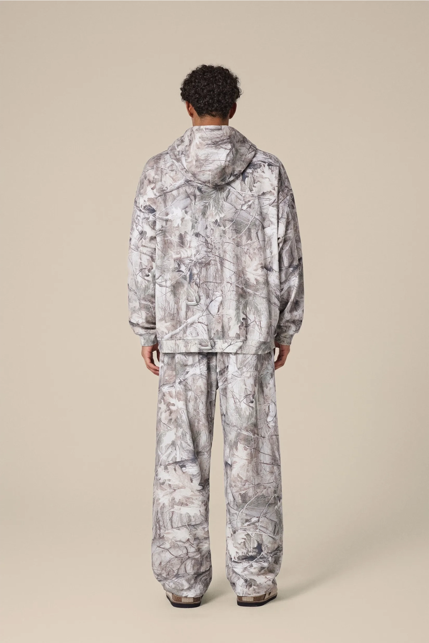 Person wearing a camouflage raincoat and pants on a beige background