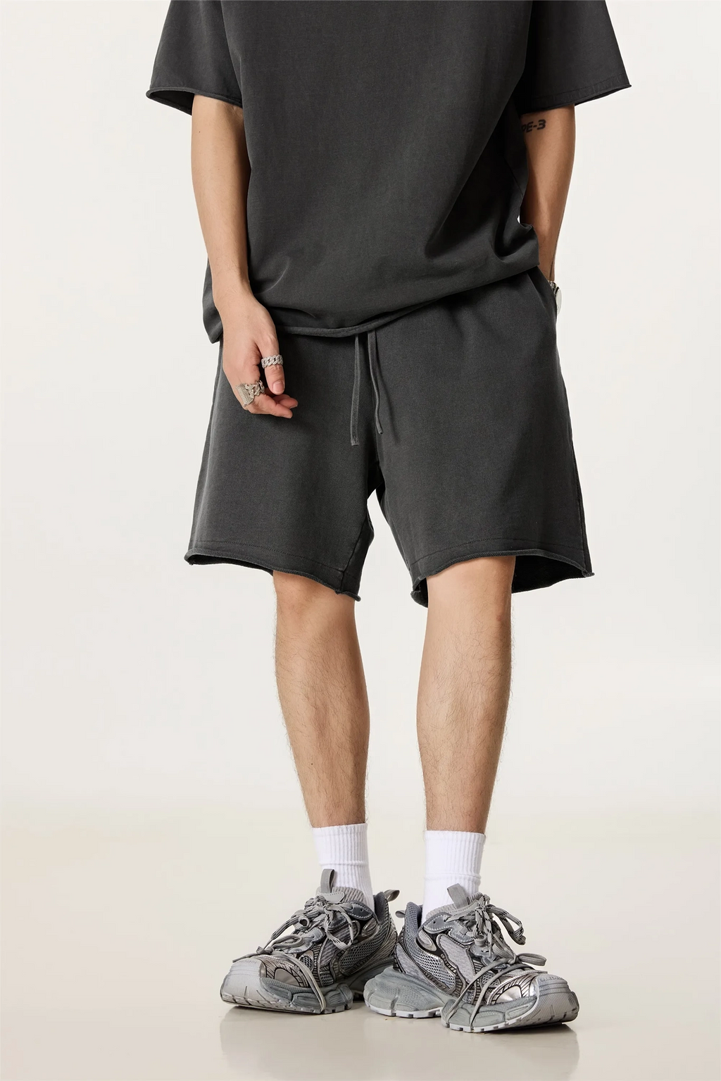 Person wearing a black t-shirt and shorts with gray sneakers on a light background