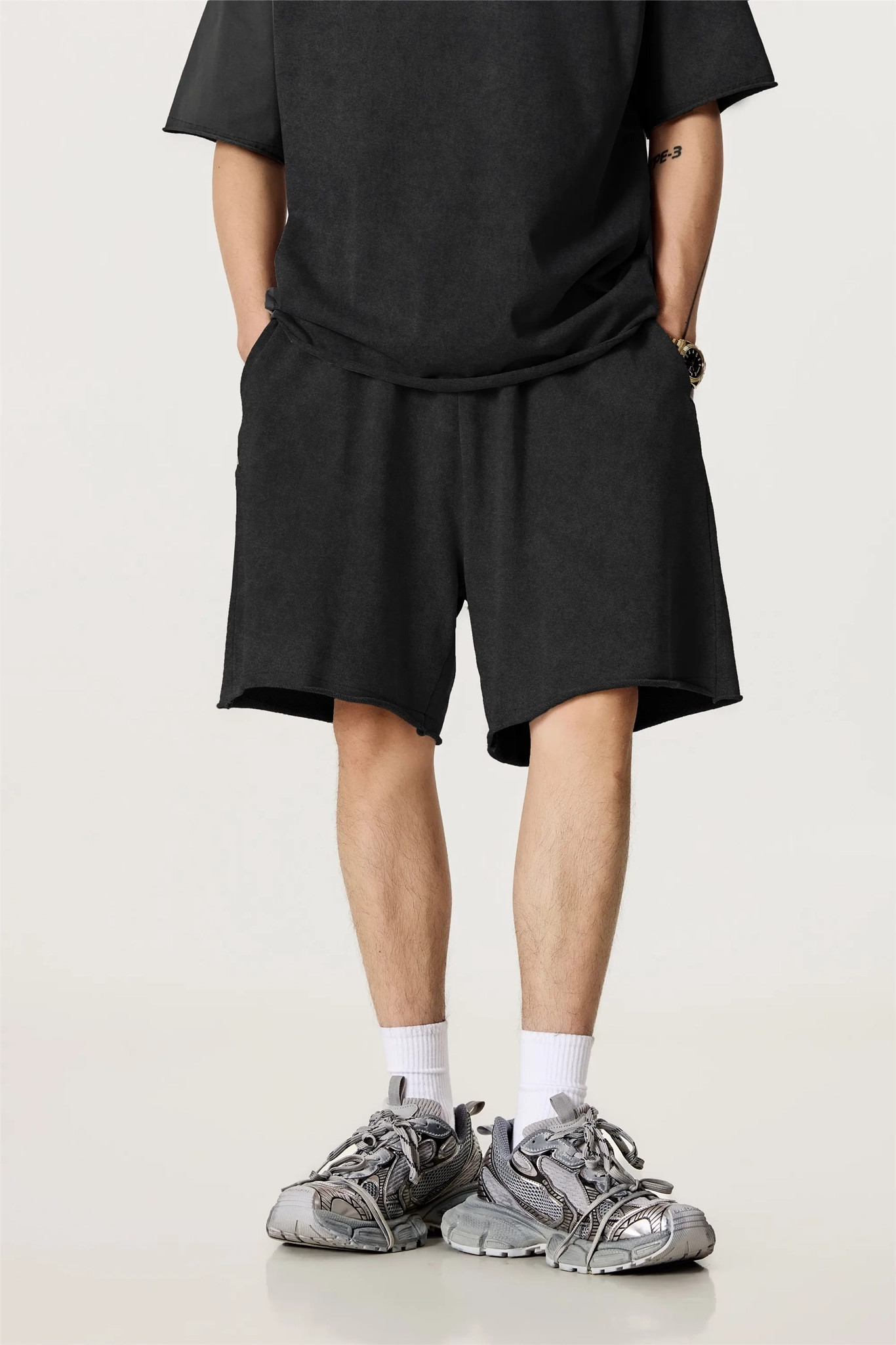 Person wearing a black outfit with shorts and sneakers on a white background
