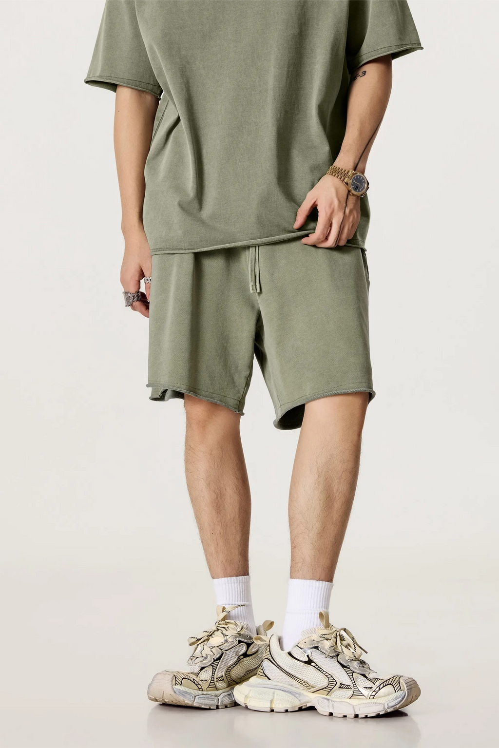 Person wearing a green t-shirt and shorts with beige sneakers on a light background