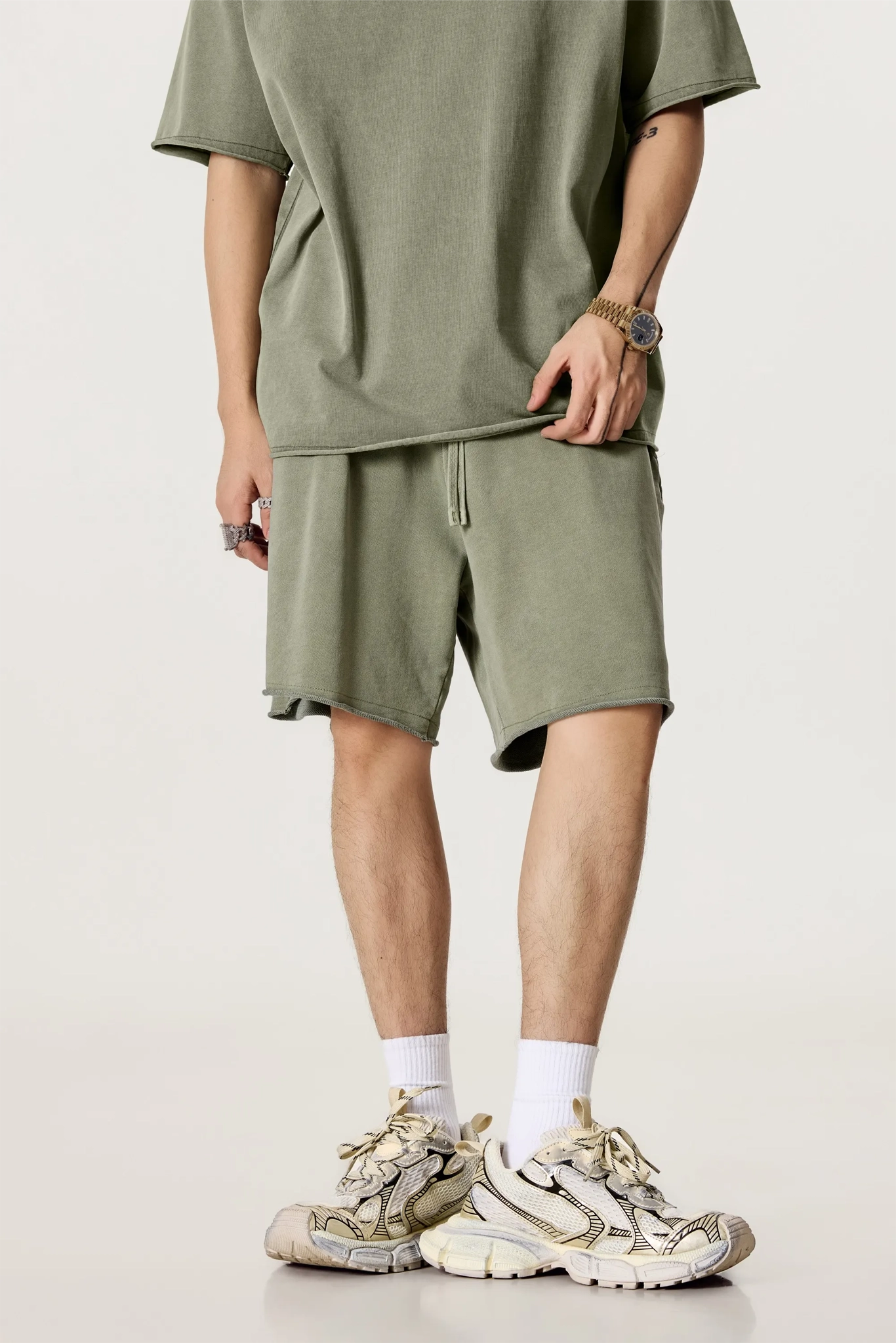 Person wearing a green t-shirt and shorts with beige sneakers on a light background