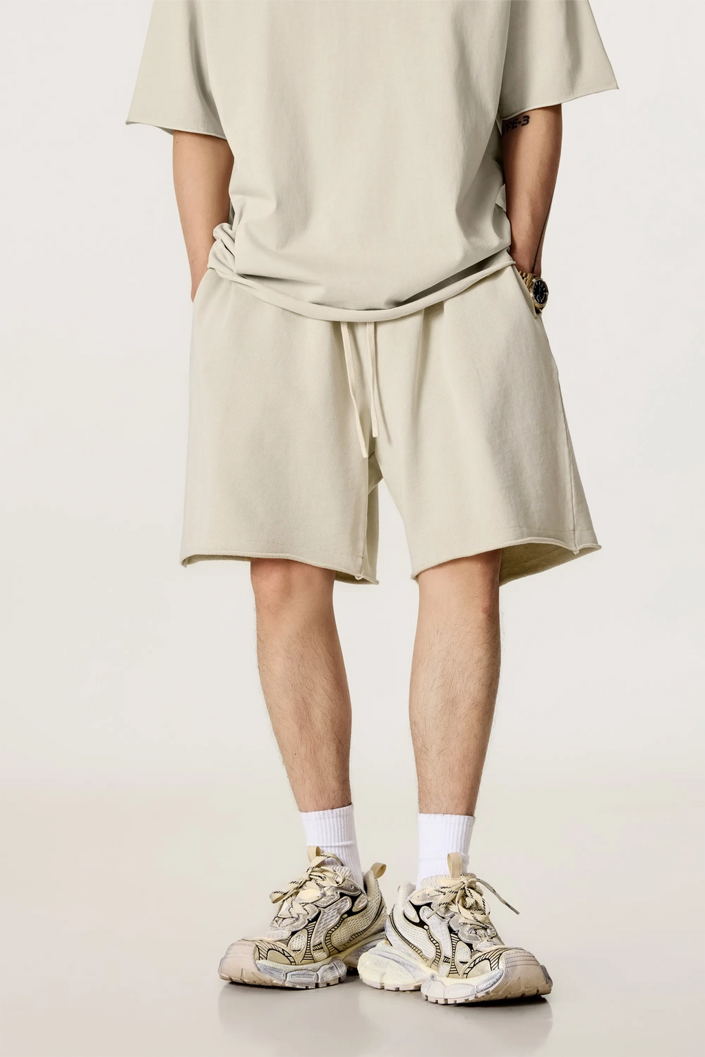 Person wearing a beige outfit with shorts and sneakers on a plain background