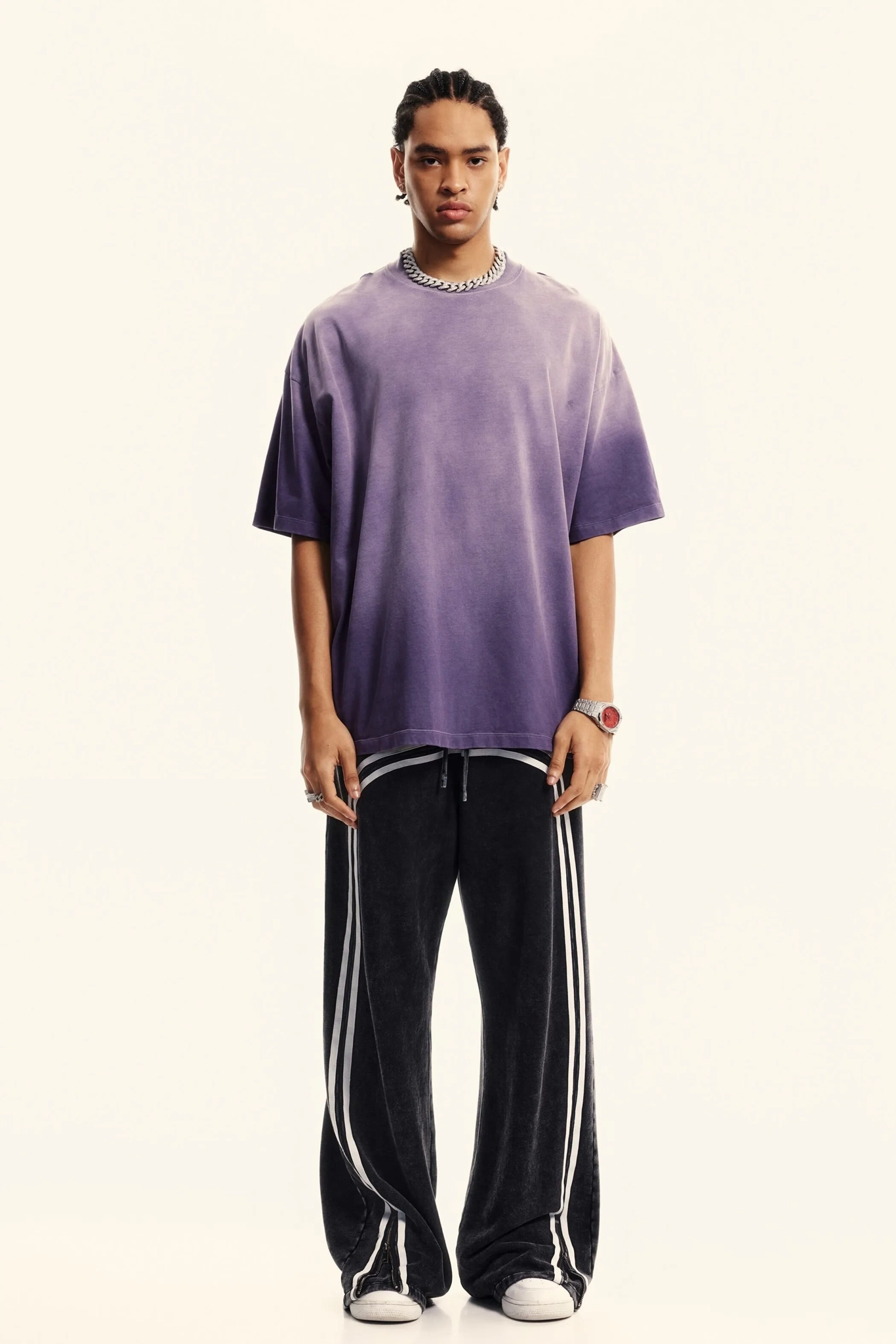 Person wearing a purple oversized t-shirt and black pants with white stripes on a white background
