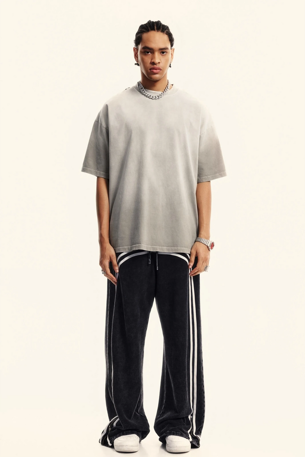 Person wearing a gray oversized t-shirt and black pants with white stripes on a white background
