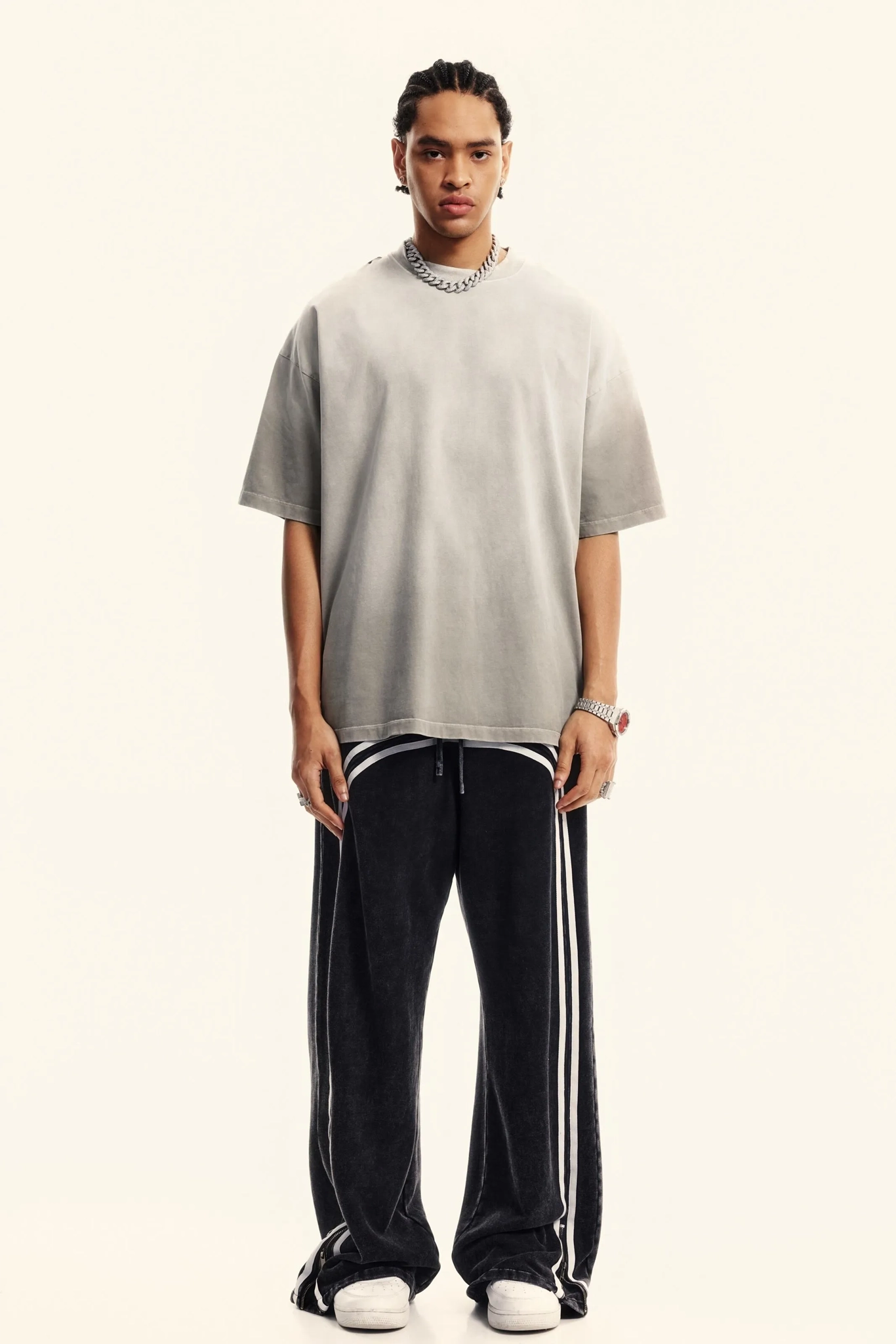 Person wearing a gray oversized t-shirt and black pants with white stripes on a white background