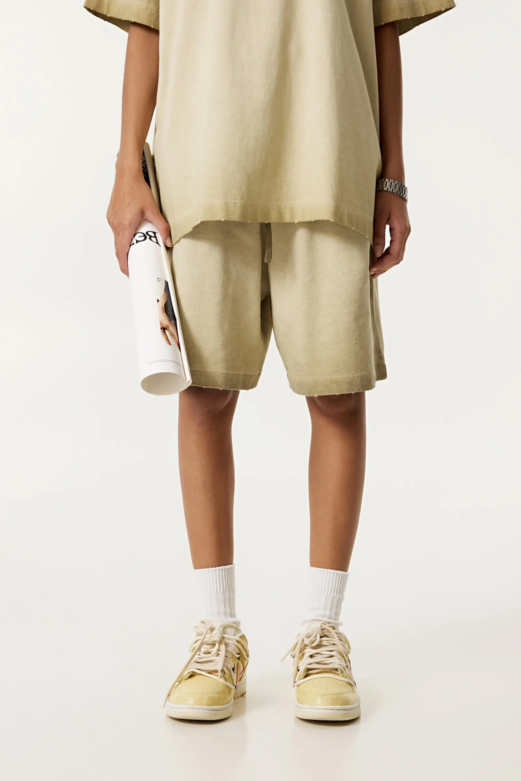 Person wearing beige outfit with shorts and sneakers on a white background