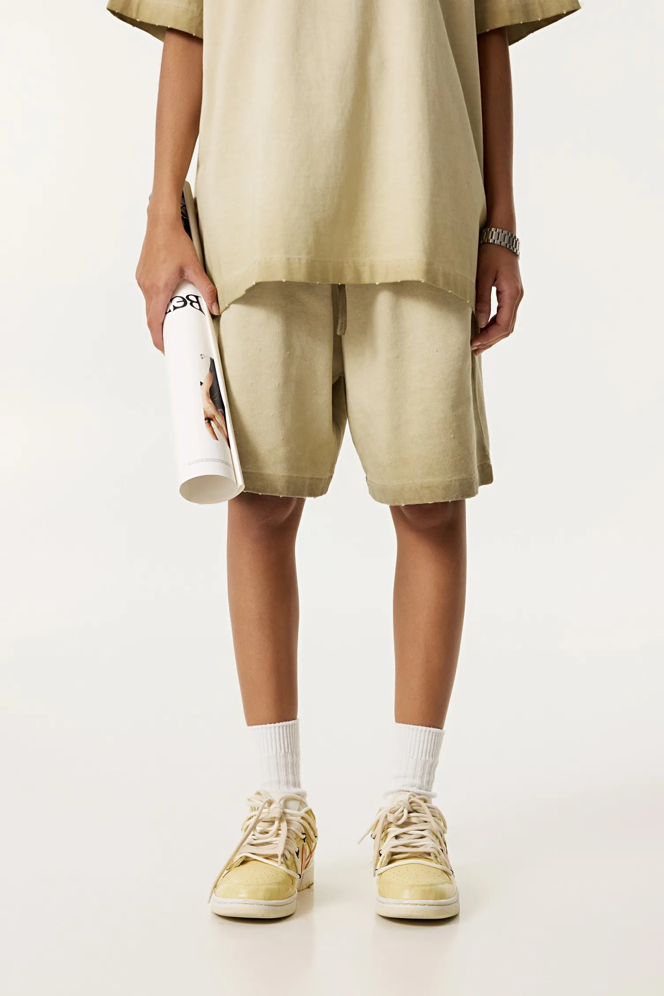 Person wearing beige outfit with shorts and sneakers on a white background