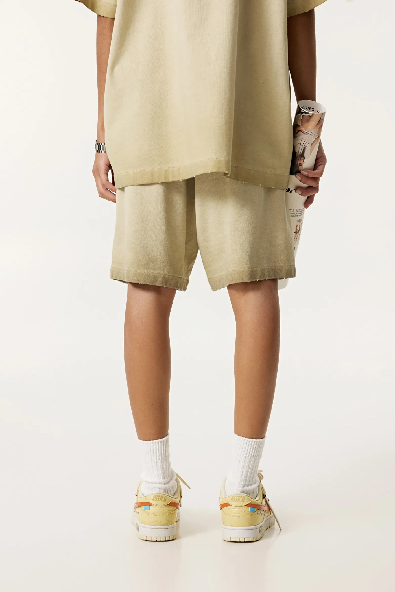 Person wearing a beige outfit with shorts and sneakers on a white background