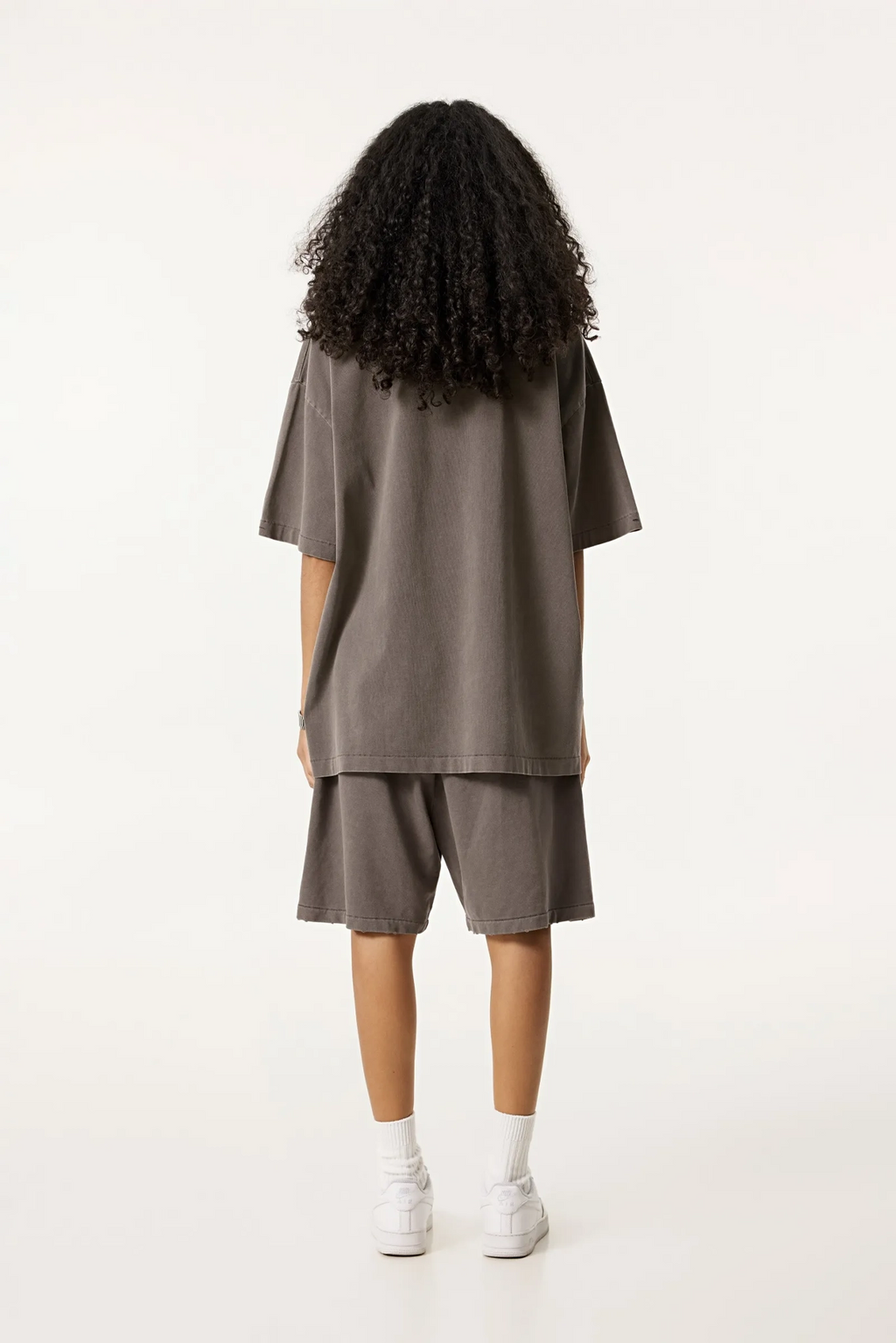 Person wearing a brown oversized t-shirt and shorts set on a white background