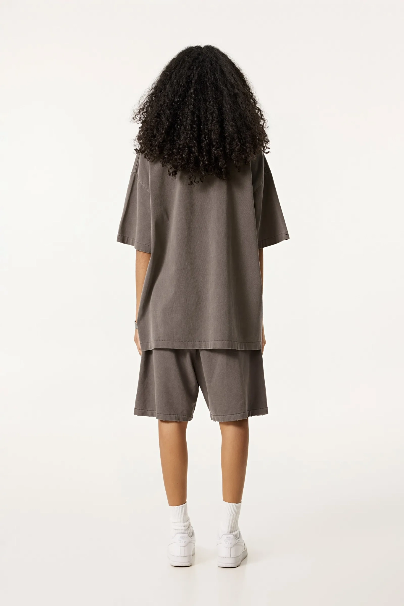 Person wearing a brown oversized t-shirt and shorts set on a white background